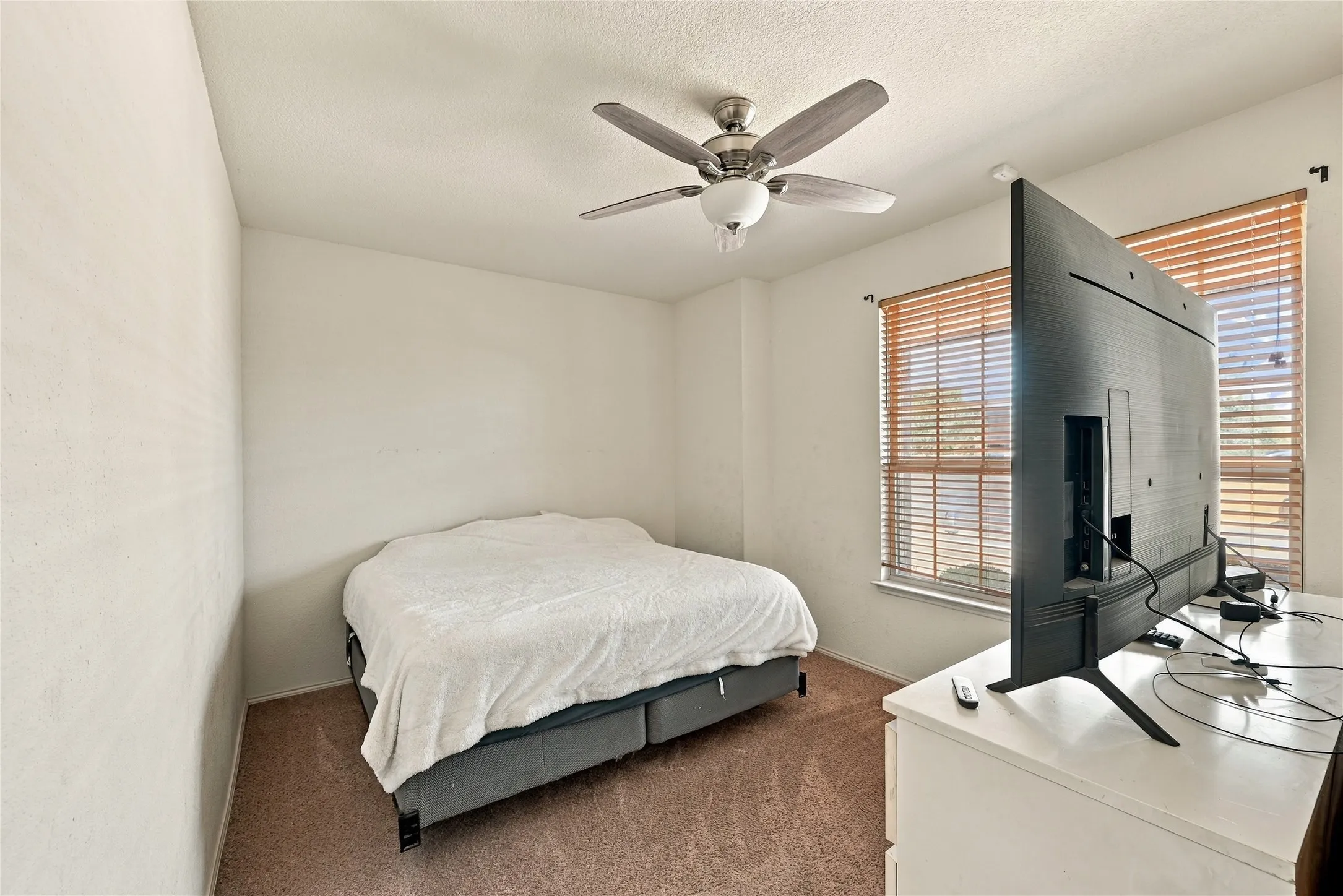 Room with ceiling fan, two windows featuring wood-finish blinds, and textured wall finishes