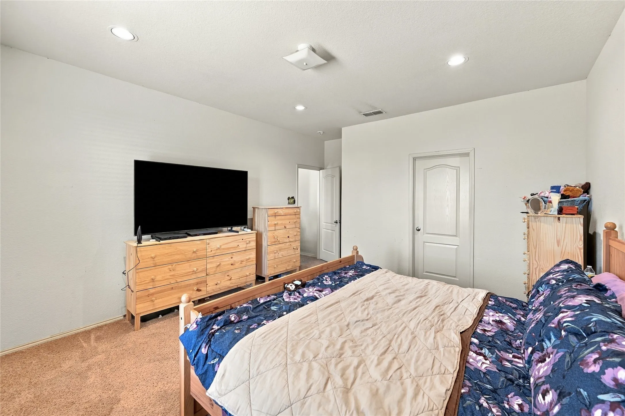 Recessed lighting illuminates a spacious room featuring wall-to-wall carpeting and white paneled doors