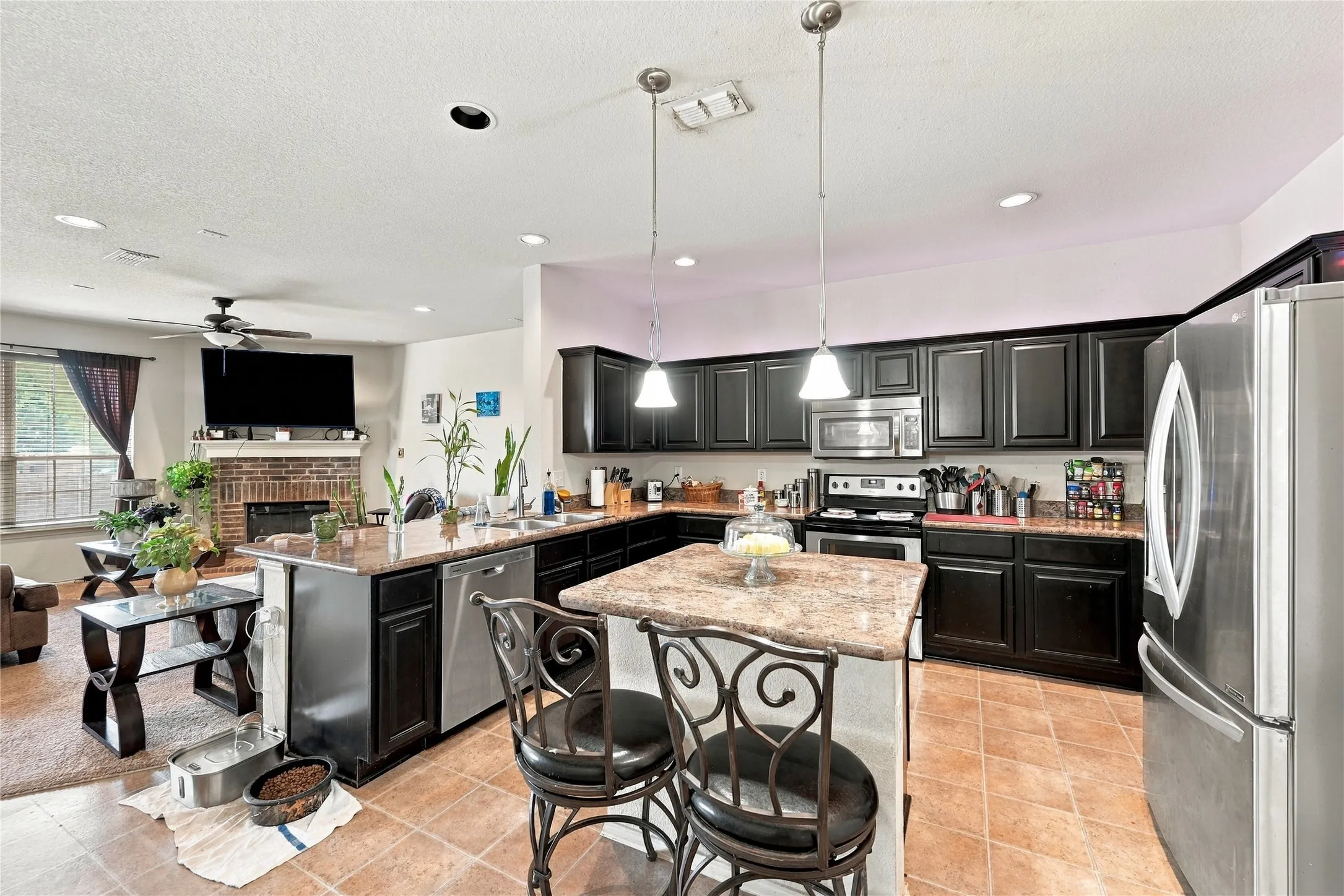 Kitchen featuring dark wood cabinetry, stainless steel appliances, stone countertops, a central island with pendant lighting, and tile flooring