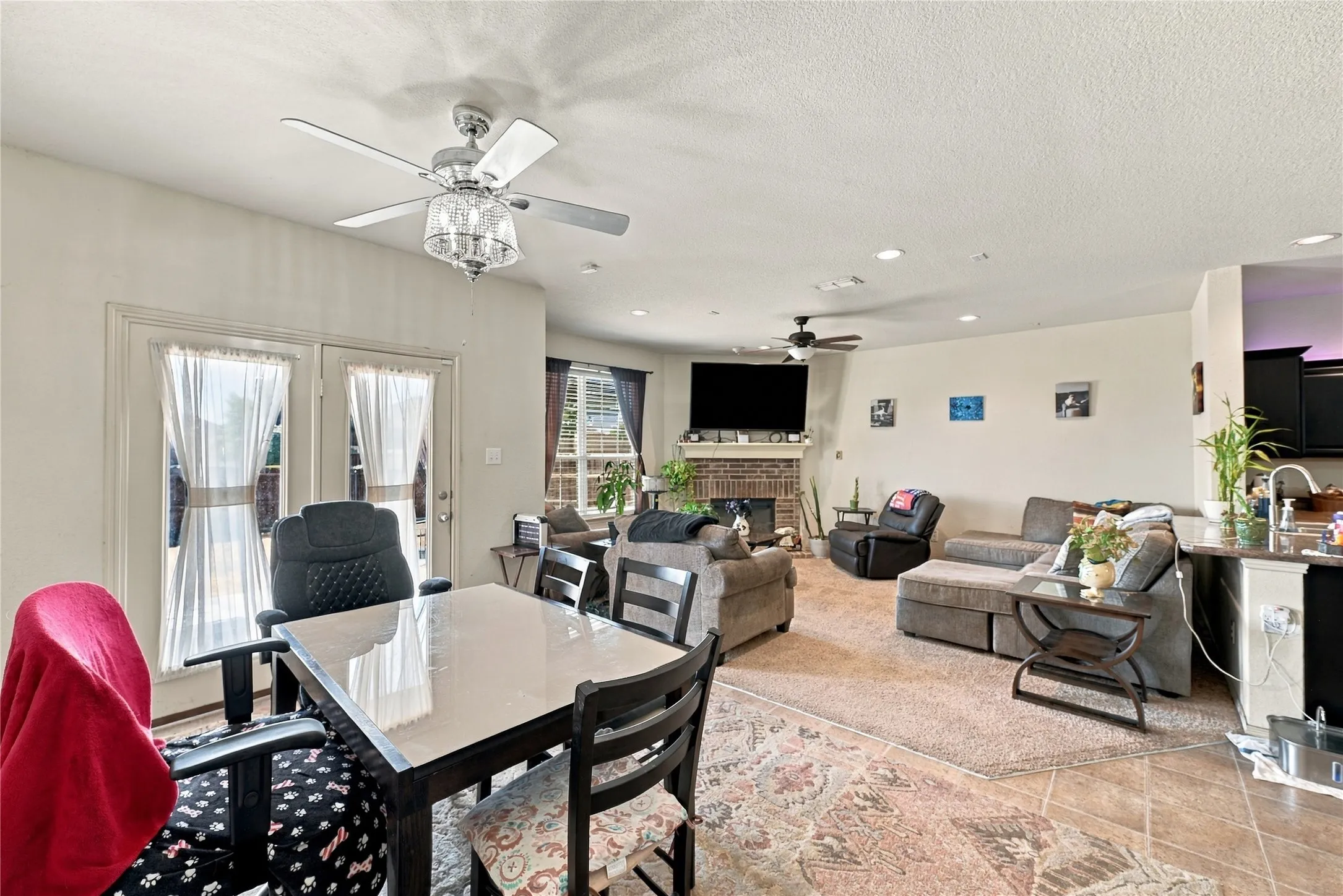 Bright interior space featuring a ceiling fan with light fixture, double glass-paneled doors, recessed lighting, a brick fireplace, and a kitchen island with a dark countertop