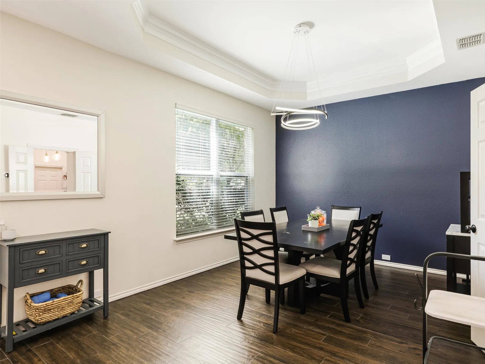 Wood-finish flooring throughout, tray ceiling with crown molding, contemporary chandelier, and a window with blinds