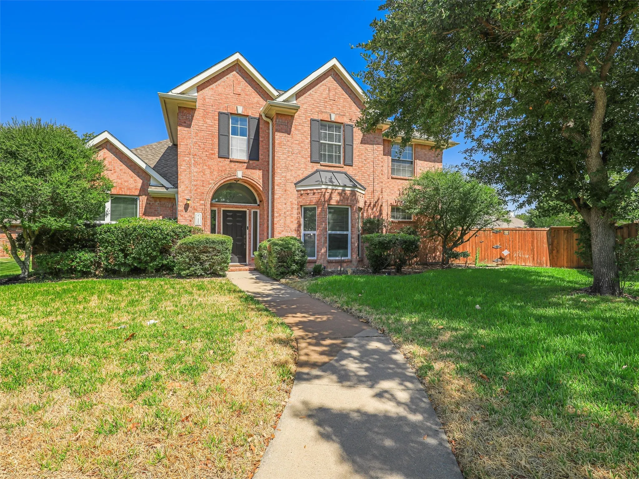 Brick exterior with multiple gables, arched entry, black paneled shutters, and established landscaping