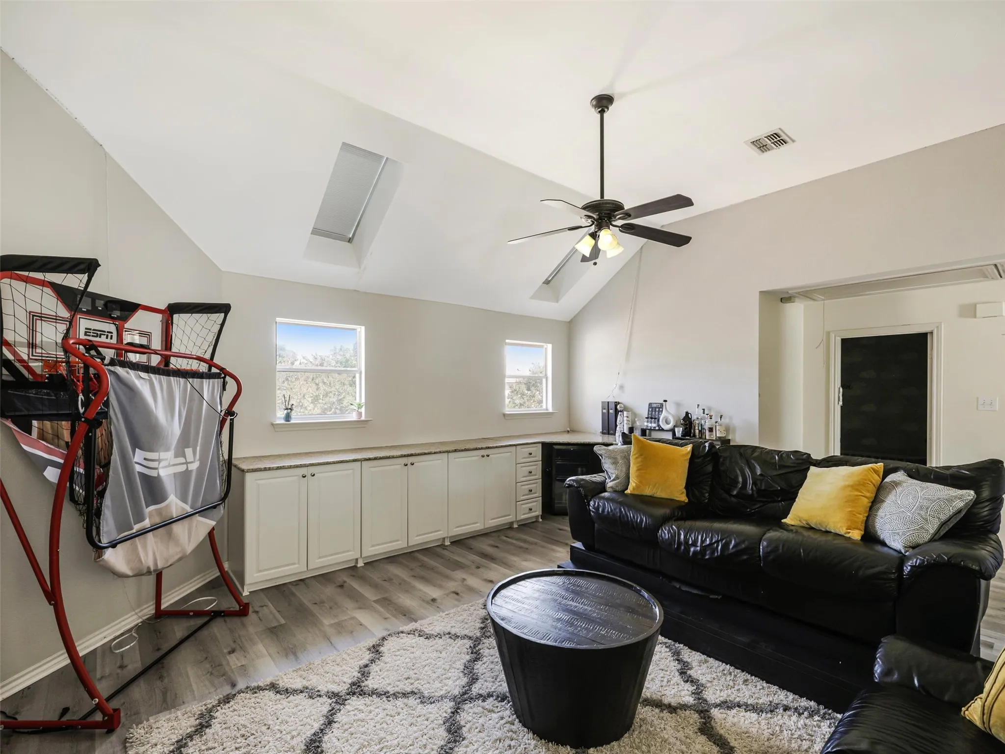 Vaulted ceiling with skylight, wood-finish flooring, ceiling fan, and built-in white cabinetry with a light-toned countertop