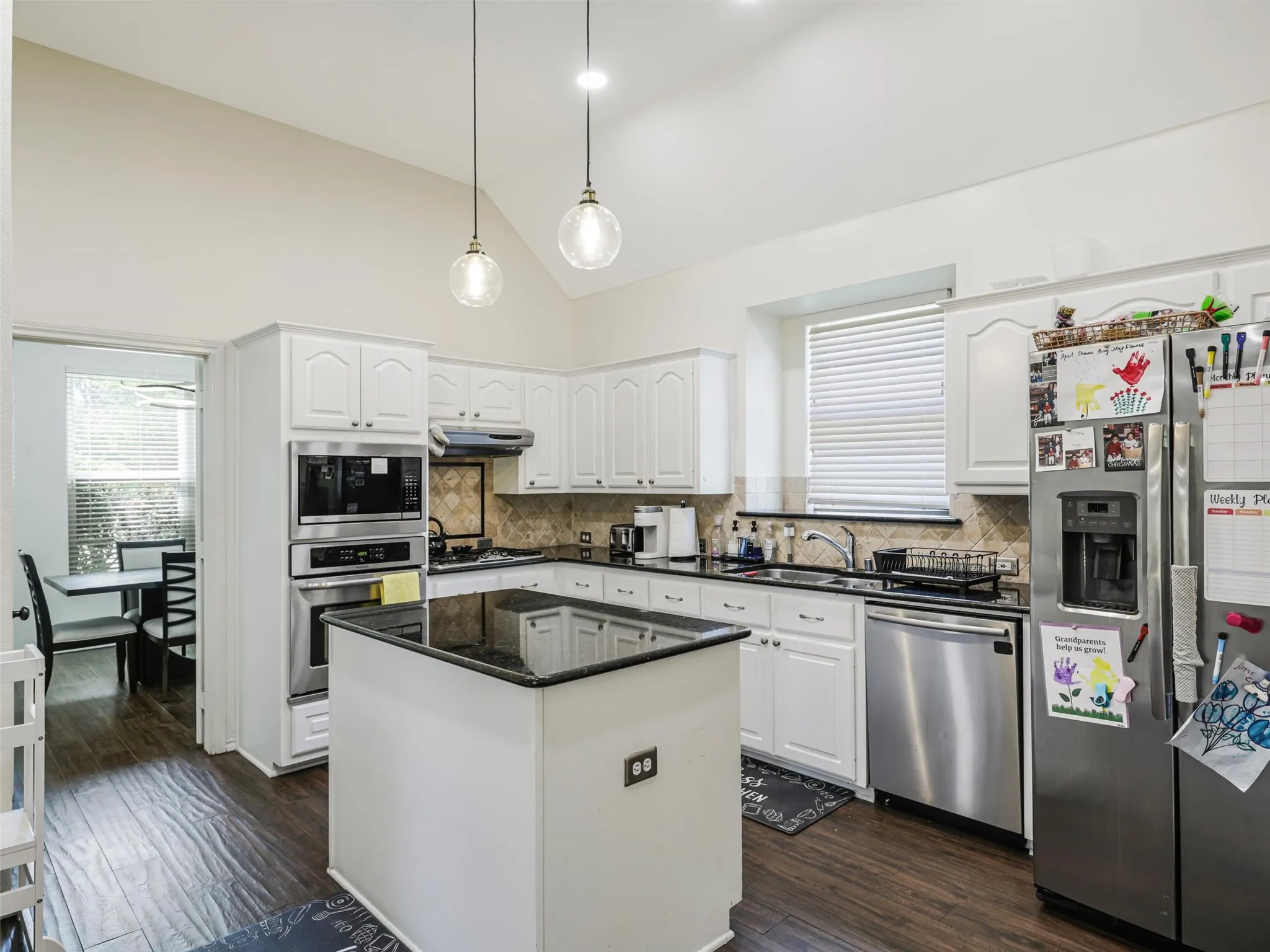 Kitchen featuring vaulted ceilings, white cabinetry, a center island with a dark countertop, stainless steel appliances, and wood-finish flooring