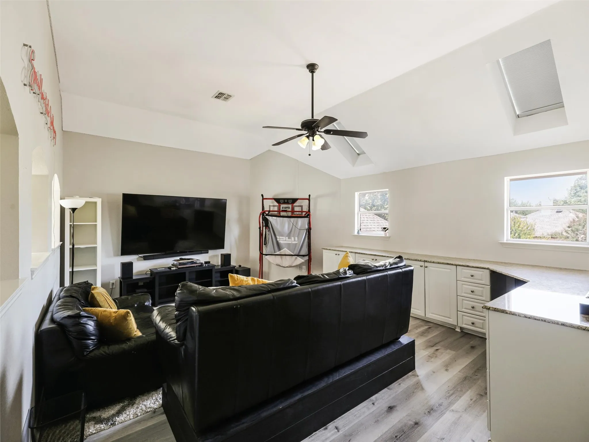 Vaulted ceiling with skylight, wood-finish flooring, ceiling fan, built-in cabinetry, and integrated countertop
