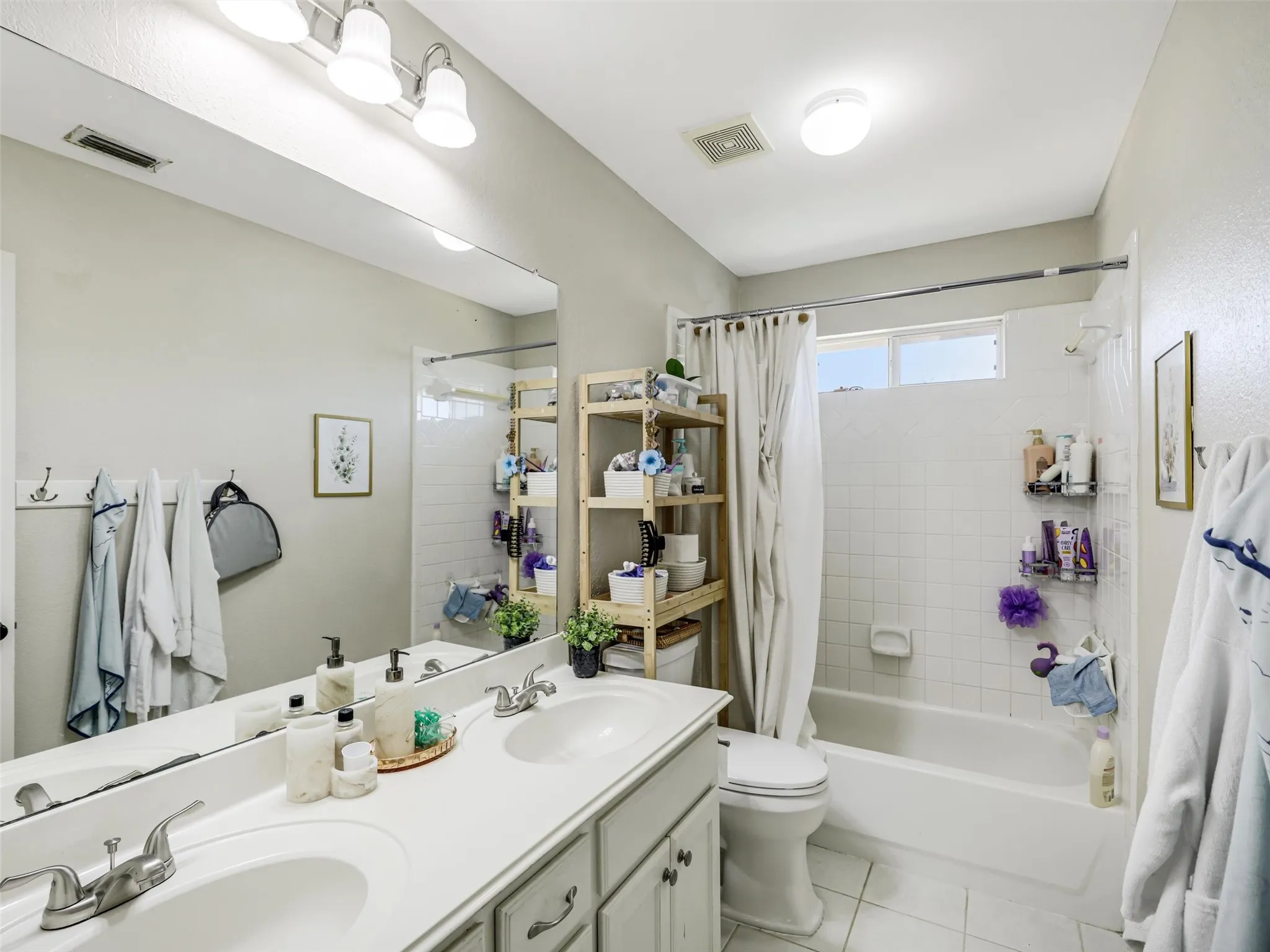 Dual vanity with integrated sinks, full-width mirror, white tile flooring, and a tub-shower combination with white subway tile surround