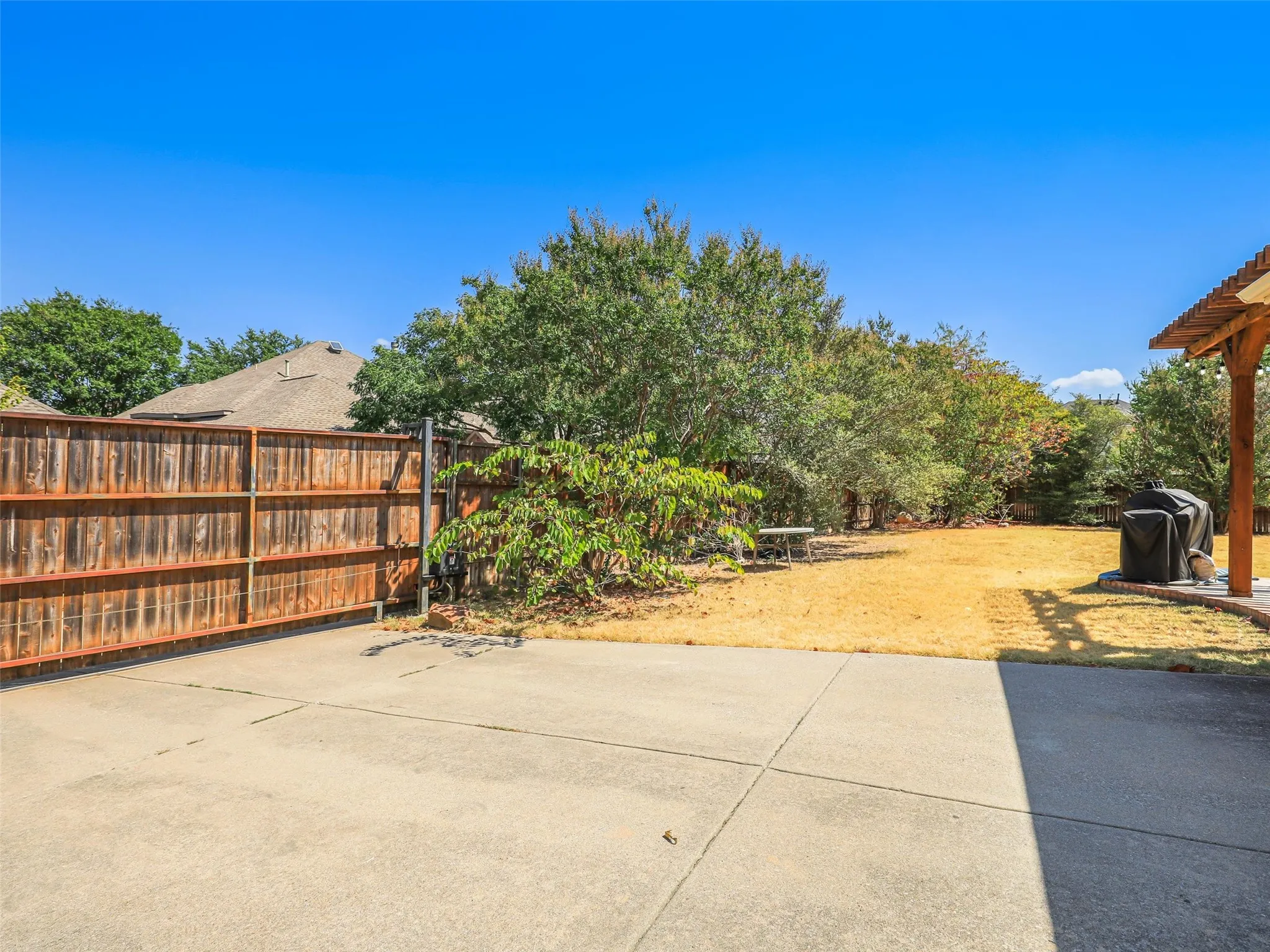 Expansive backyard with a concrete patio, wood fence, and mature trees