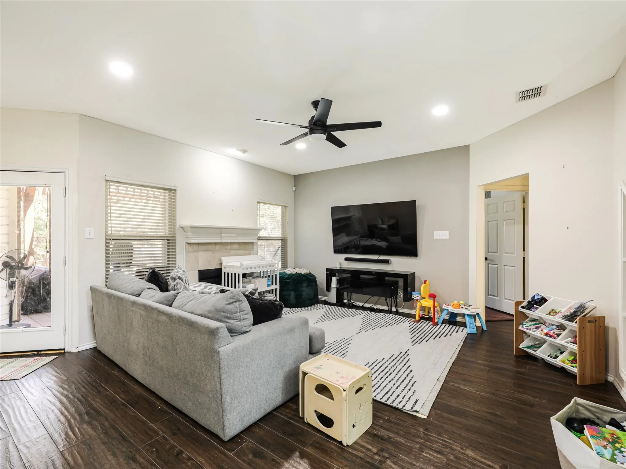 Vaulted ceiling with recessed lighting, wood-finish flooring, and a fireplace with a stone surround