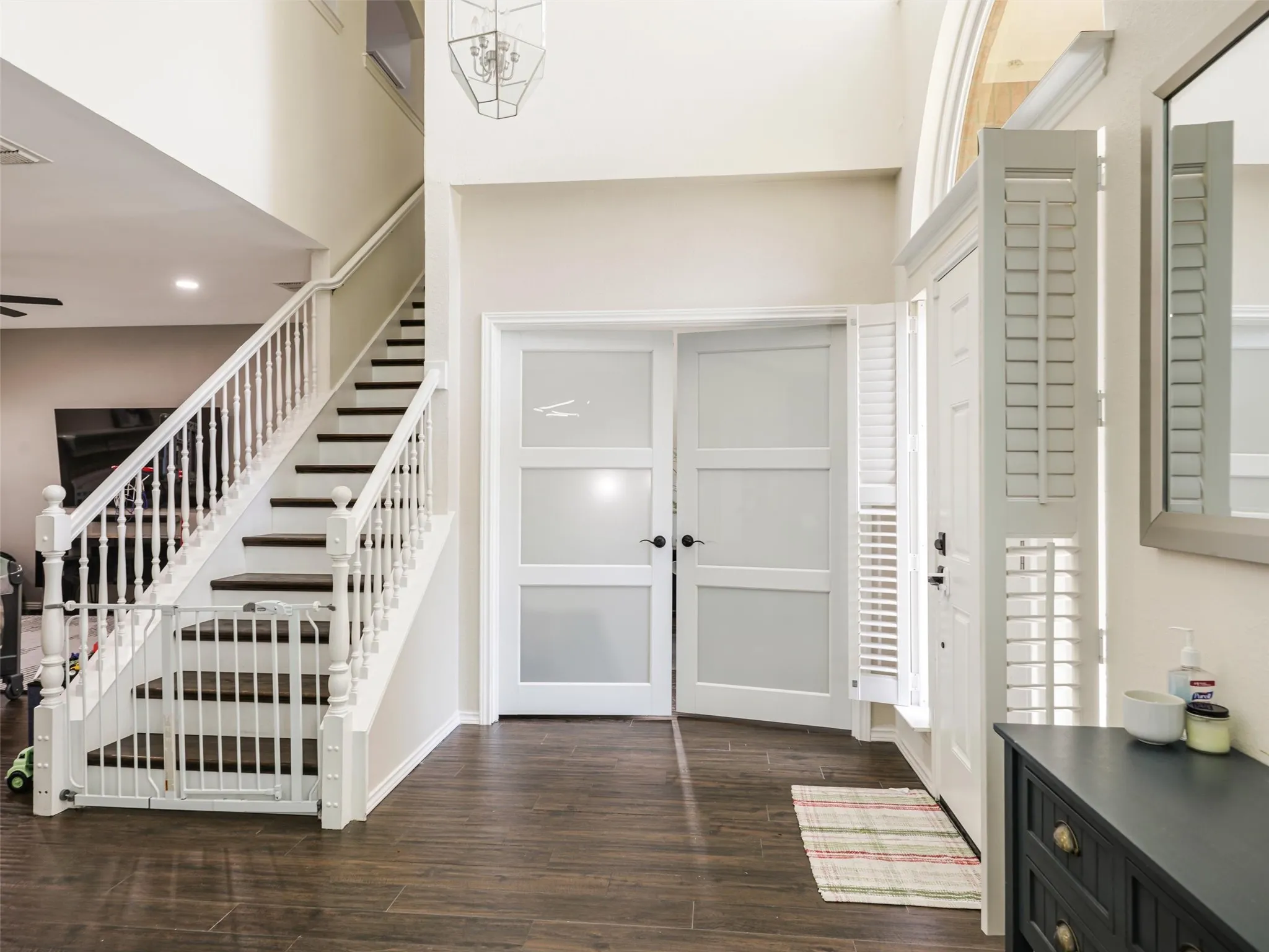 Two-story entry with wood-finish flooring, a white spindle staircase with dark treads, and a modern chandelier