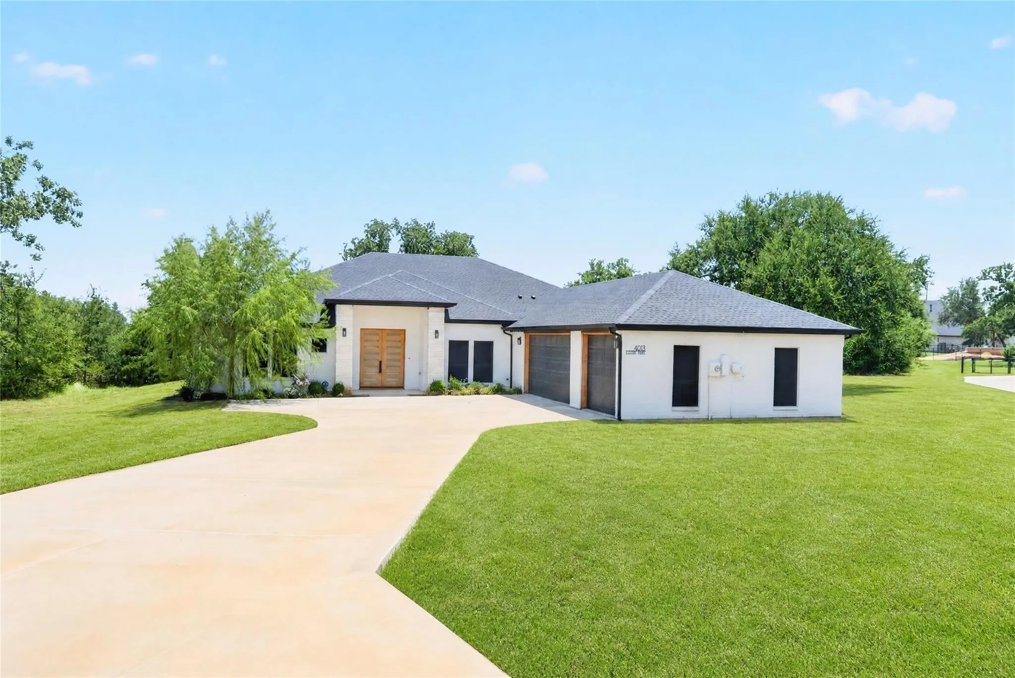 Contemporary architecture with a light-colored exterior, an expansive driveway, a dark-pitched roof, and multiple garage doors