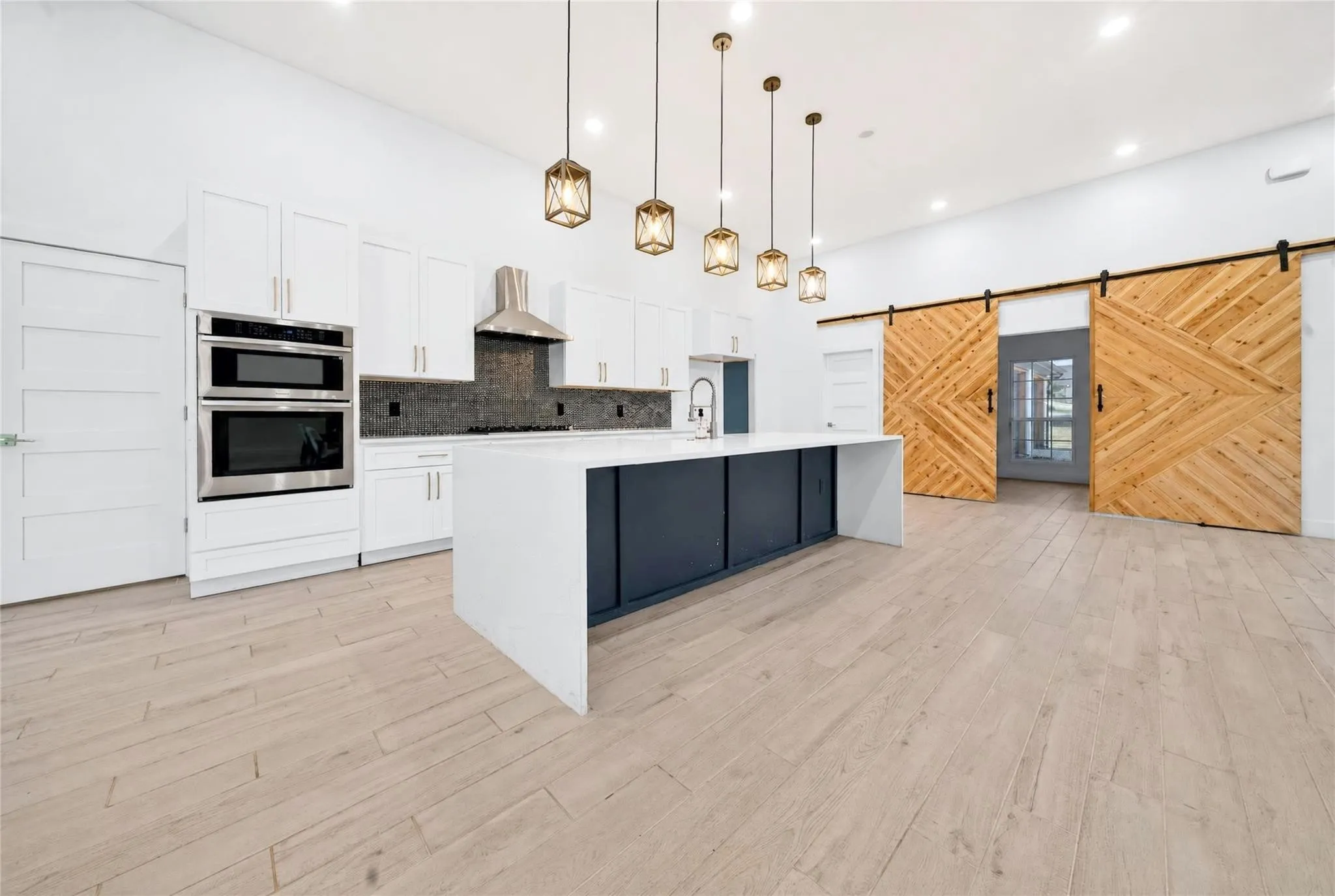 Kitchen featuring white cabinetry, stainless steel appliances, a dark tile backsplash, a large center island with a sink, and light wood-finish flooring