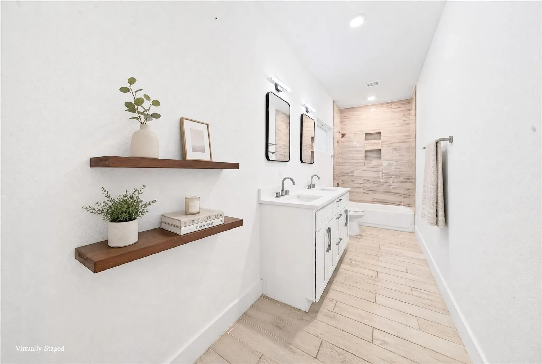 Dual floating wood shelves, white dual vanity with undermount sinks, chrome fixtures, rectangular framed mirrors, and a tiled shower with recessed niches