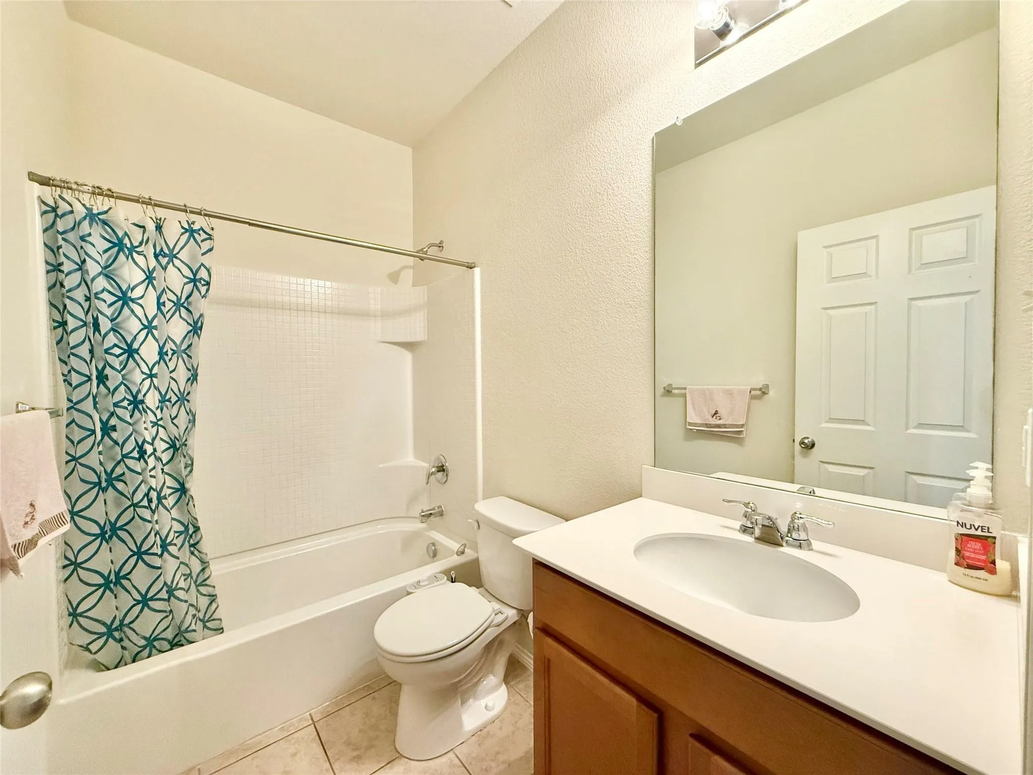 Tub and shower combination with a single-handle faucet, vanity with integrated sink, and a large wall-mounted mirror