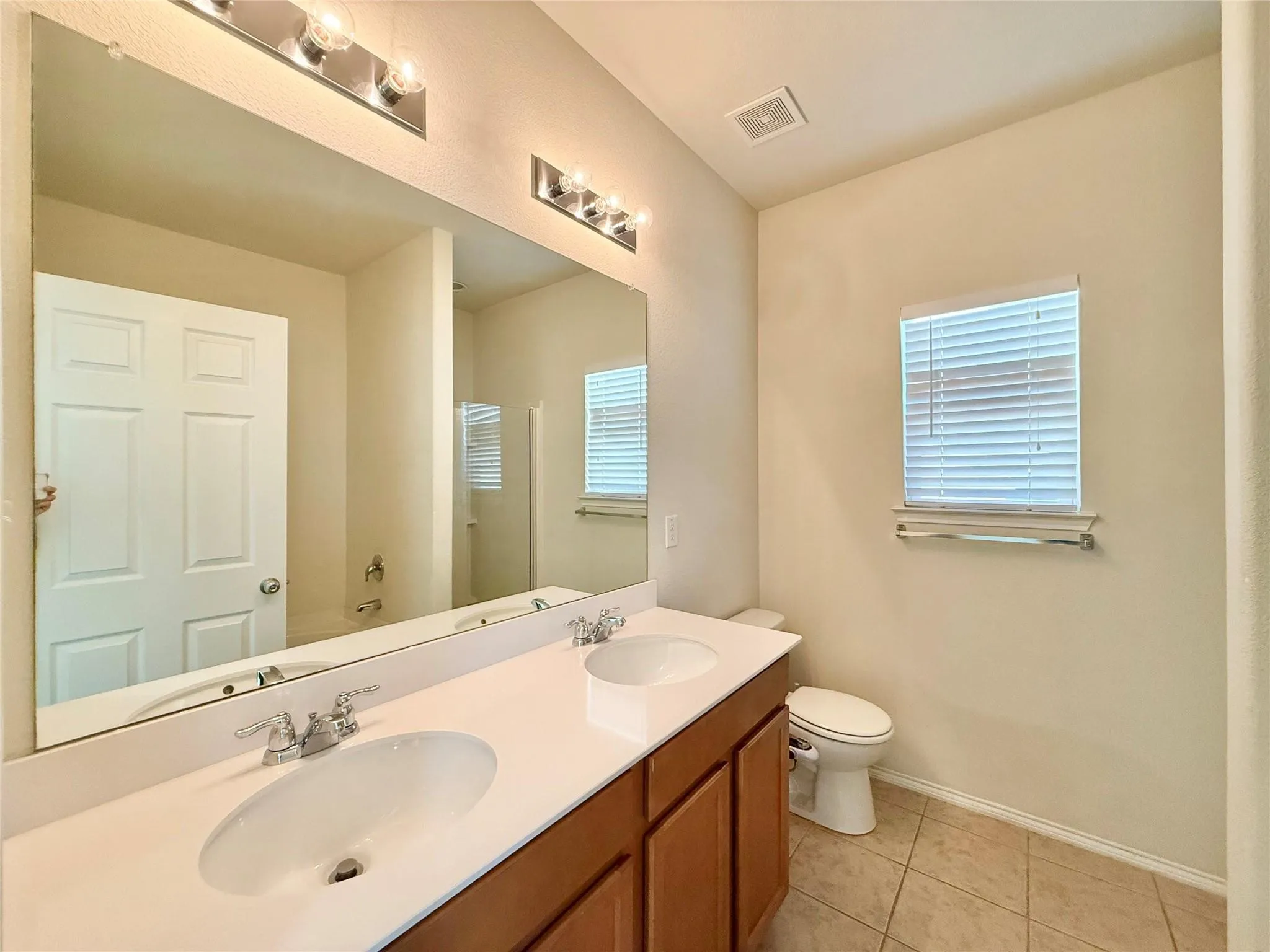 Dual vanity with undermount sinks, wood-finish cabinetry, and a large wall-mounted mirror