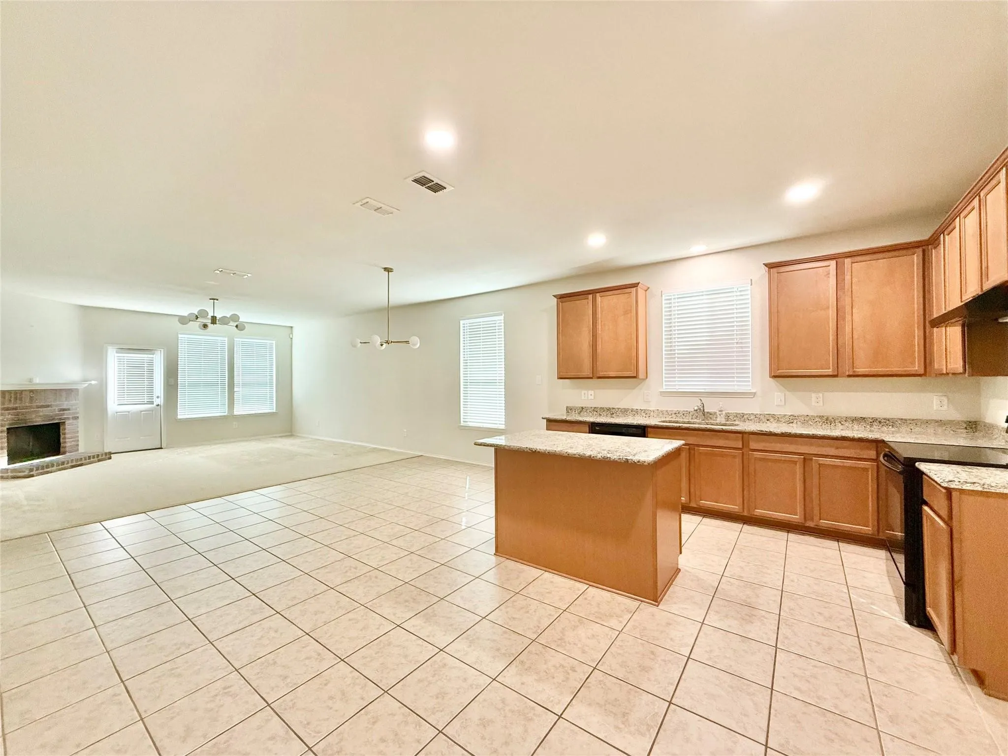 Open-concept kitchen and living area featuring tile flooring, a kitchen island, light wood-finish cabinetry, and a brick fireplace