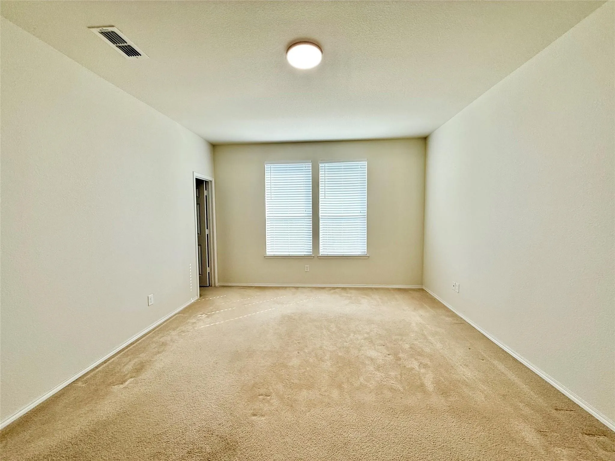 Neutral-toned walls and carpeting, two windows with blinds, and a flush-mount ceiling light fixture