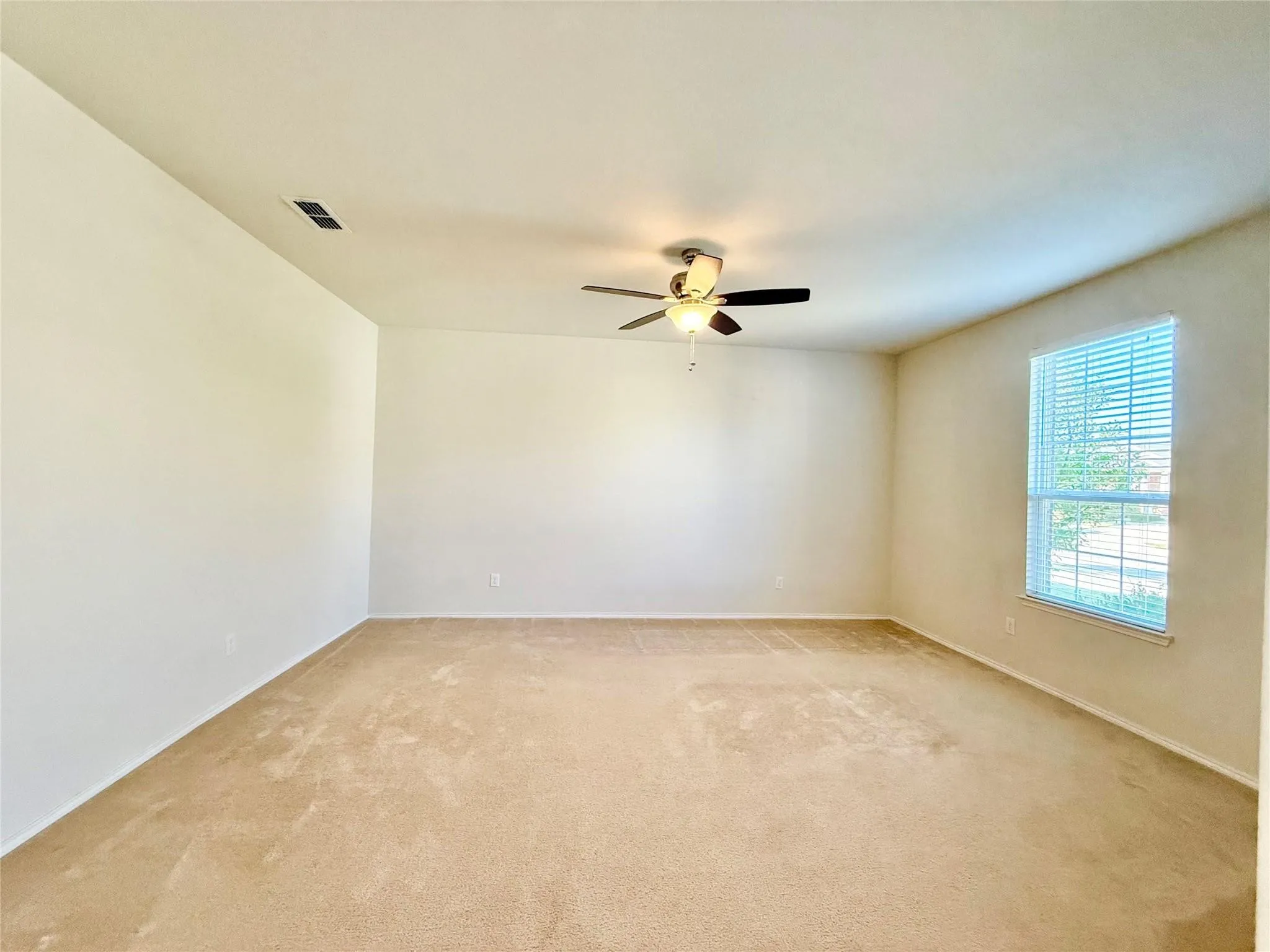 Expansive room featuring neutral-toned carpeting and walls, a ceiling fan with integrated lighting, and a window with blinds
