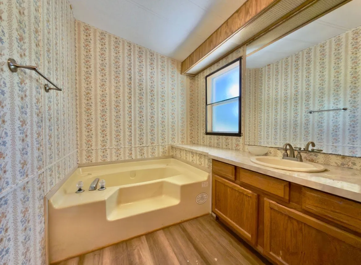 Corner soaking tub, wood-finish flooring, single vanity with integrated sink, and window