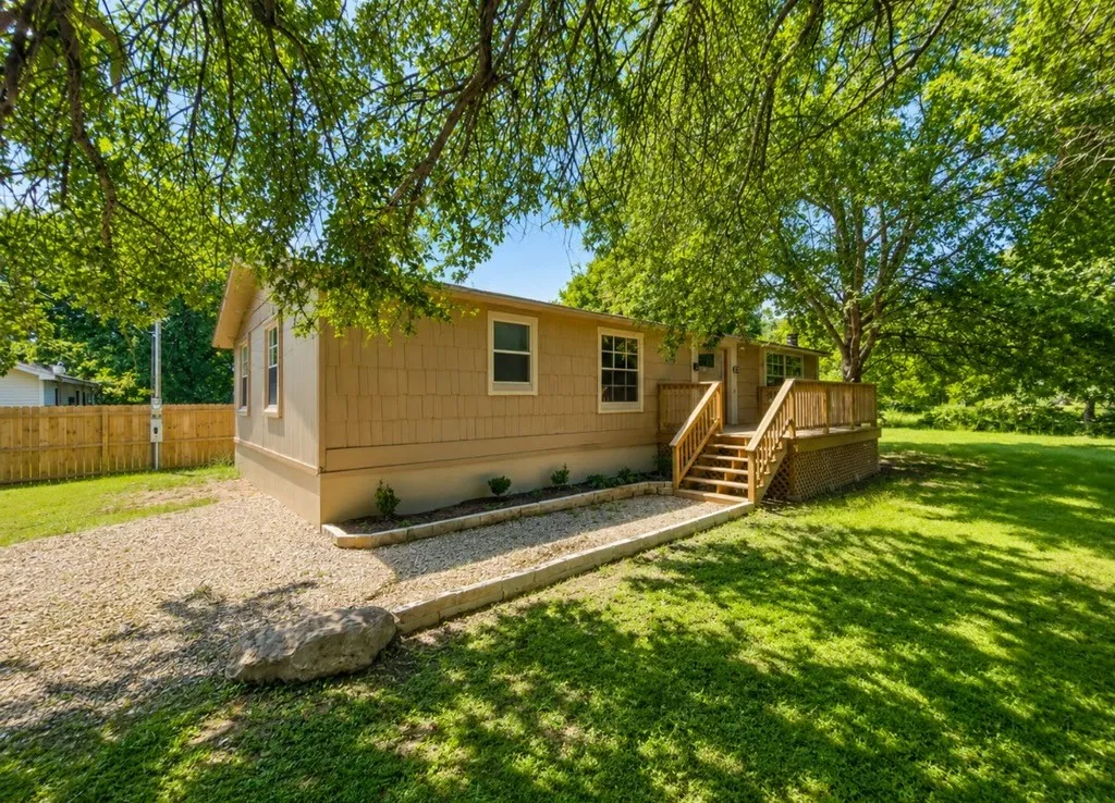 Exterior featuring neutral-toned siding, a gravel driveway, a wooden deck with railing, and a manicured lawn