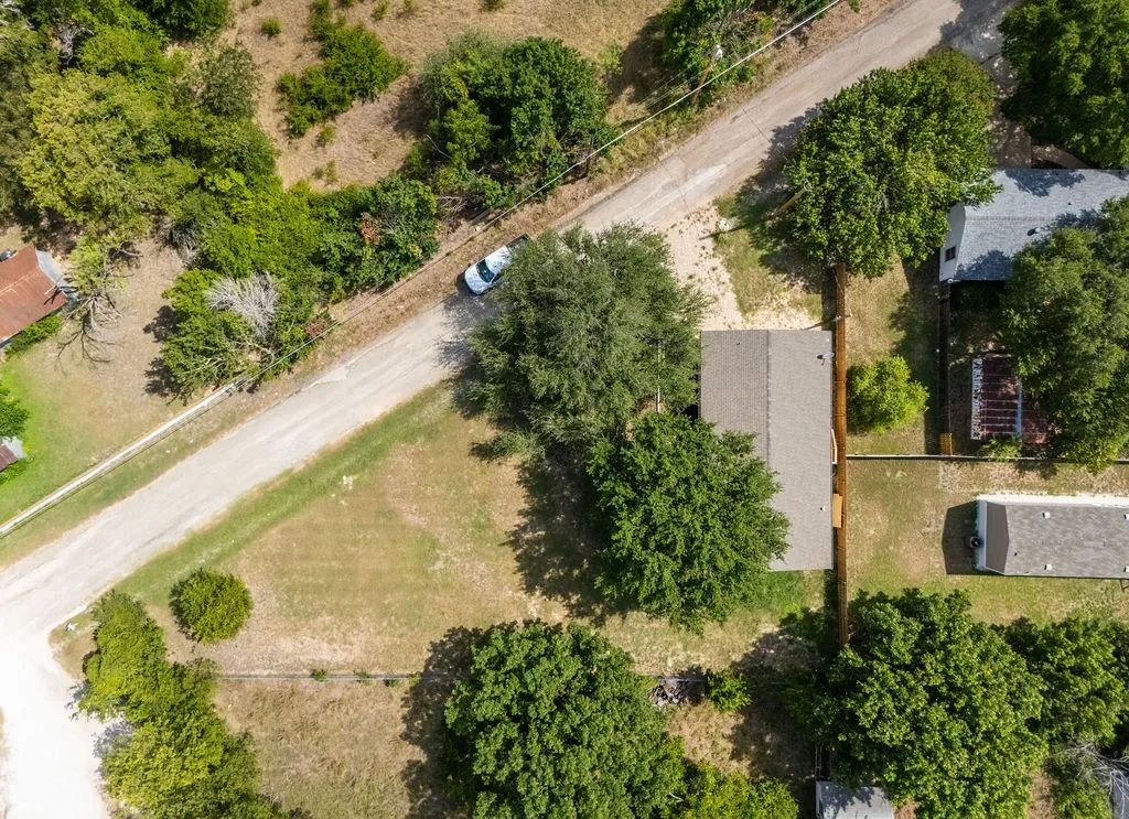 Aerial perspective showcasing a parcel of land with mature trees and a residential structure featuring a gabled roof