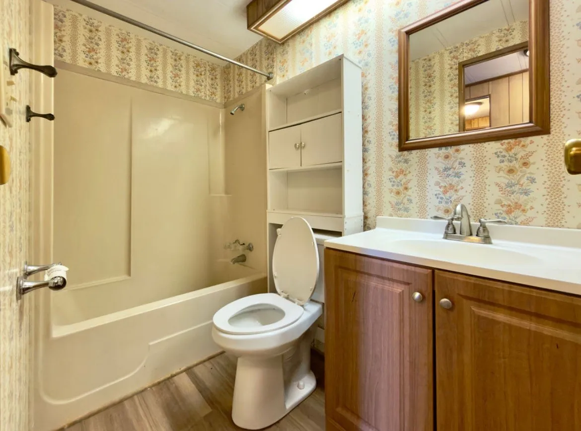 Wood-finish flooring, integrated tub and shower, vanity with wood cabinetry, and a framed mirror