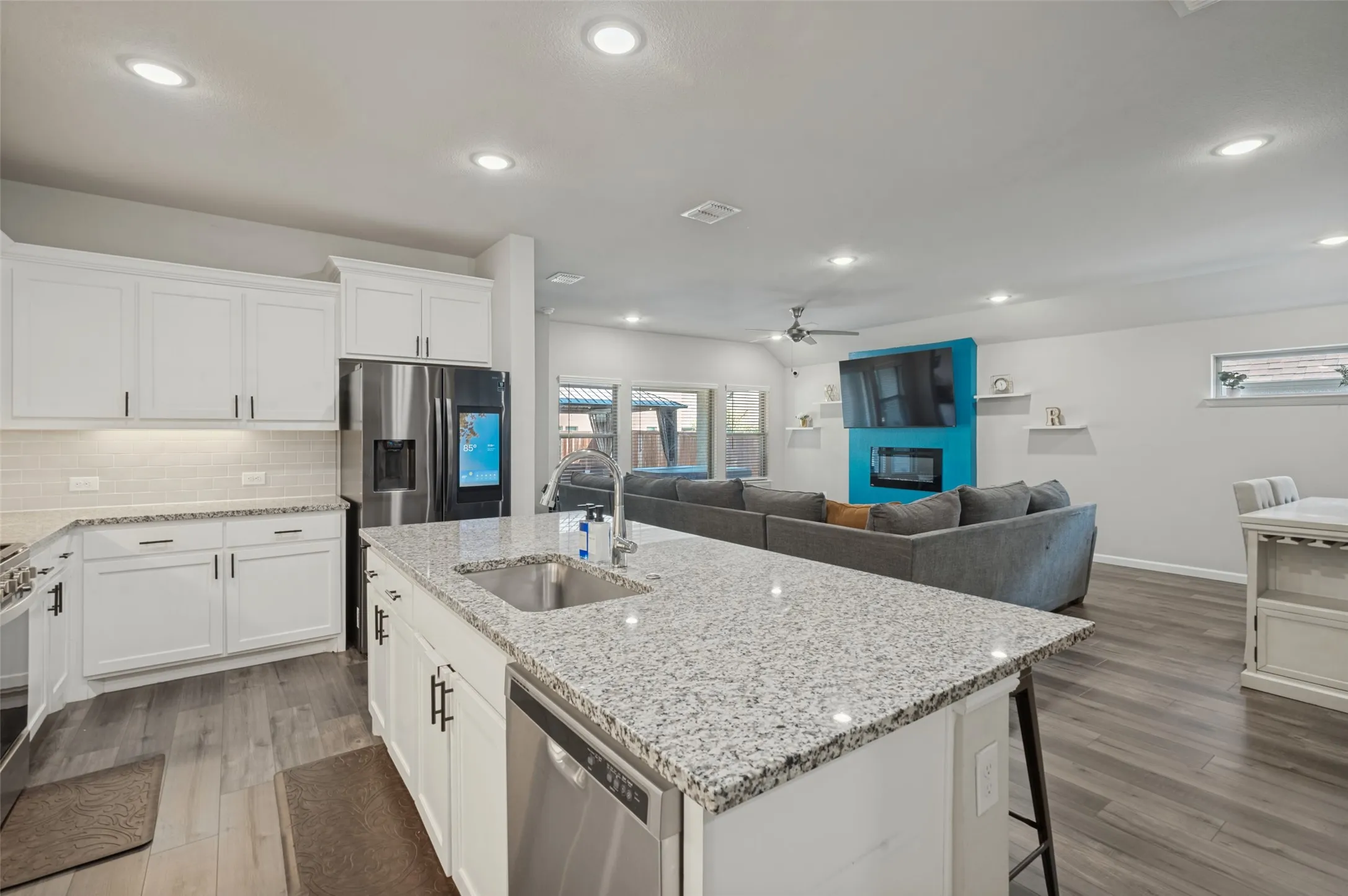 White cabinetry, stainless steel appliances, granite countertops, wood-finish flooring, and recessed lighting