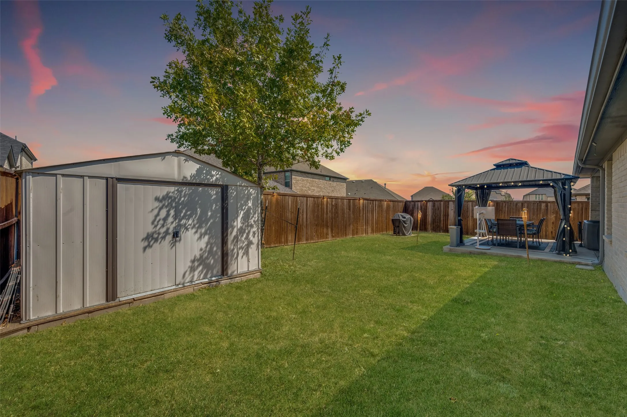 Expansive backyard with a metal storage shed, wood fence, and a patio area featuring a gazebo