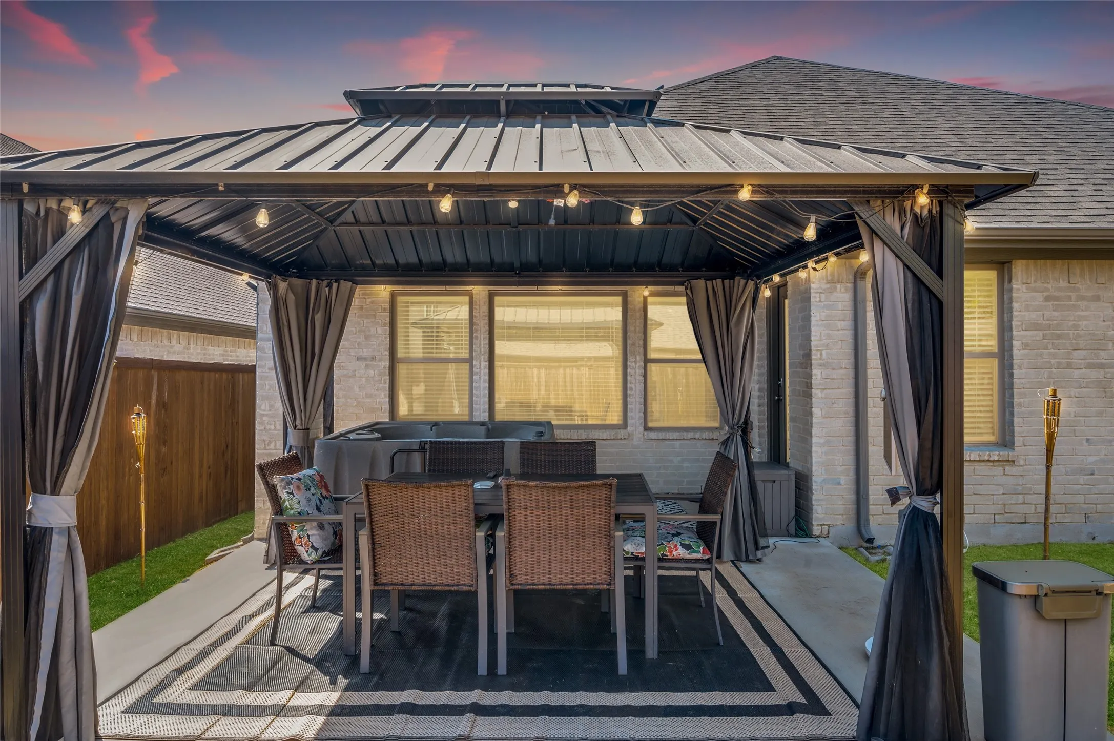 Patio area featuring a dark metal gazebo with string lighting, privacy curtains, and concrete hardscaping