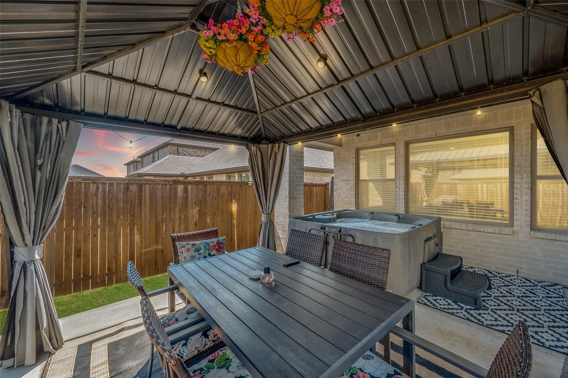 Covered patio with a metal roof and string lighting, featuring a built-in hot tub, concrete patio, and a privacy fence