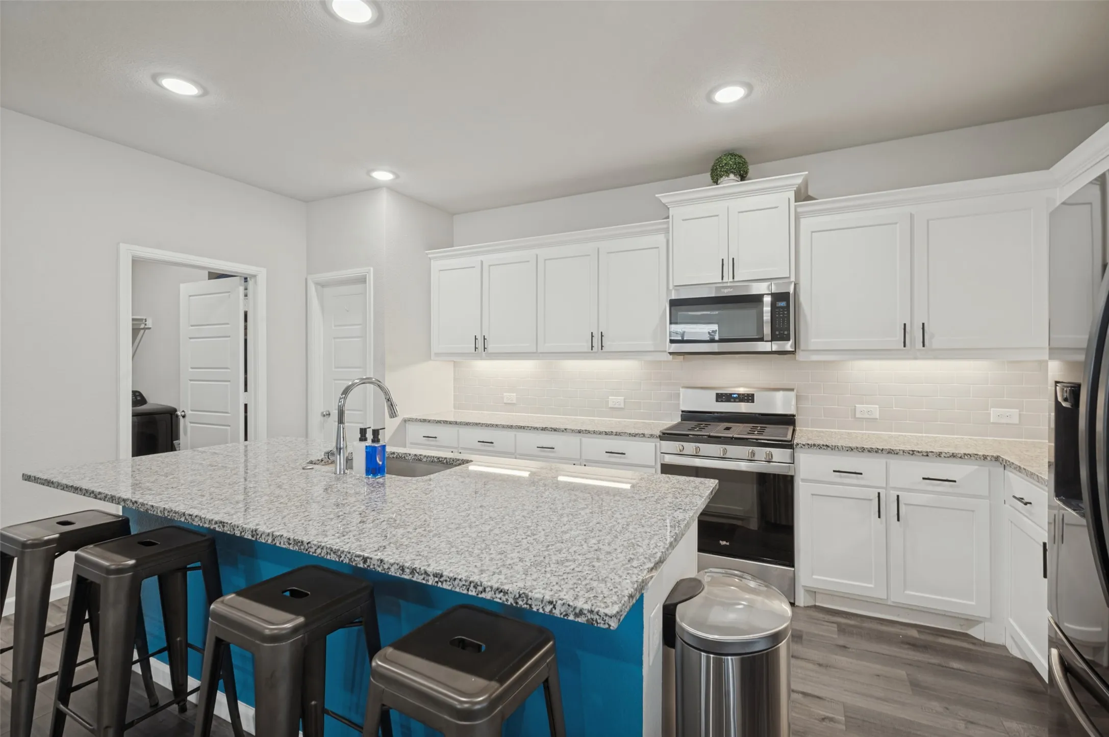 Kitchen featuring a central island with a sink and seating, white cabinetry, stainless steel appliances, granite countertops, and wood-finish flooring
