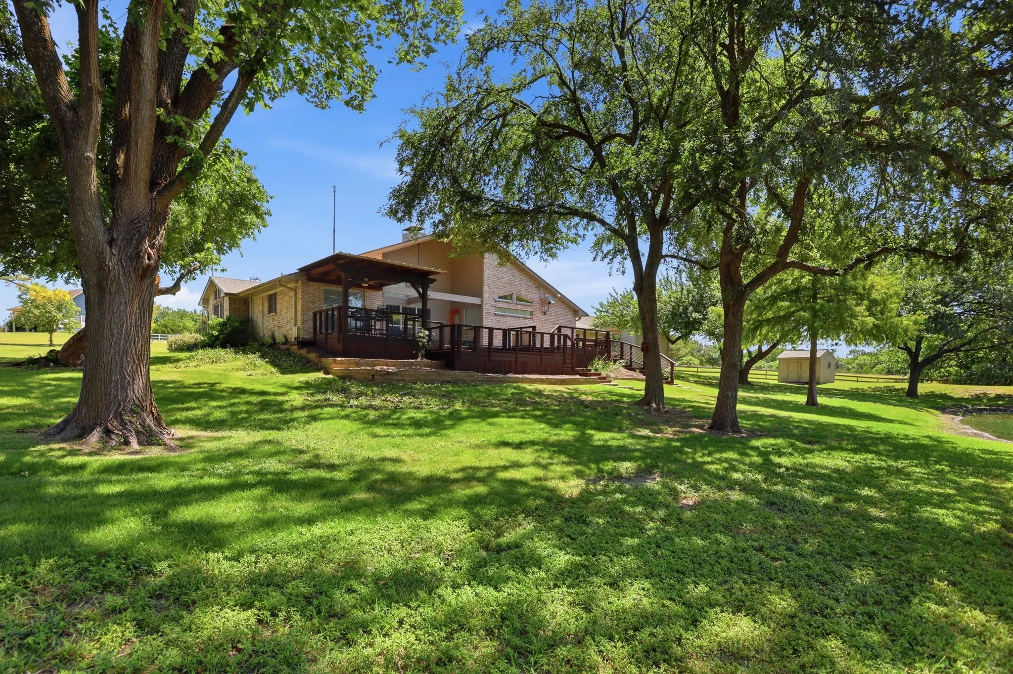 Expansive backyard with a manicured lawn, mature trees, and a multi-level wood deck featuring a covered patio