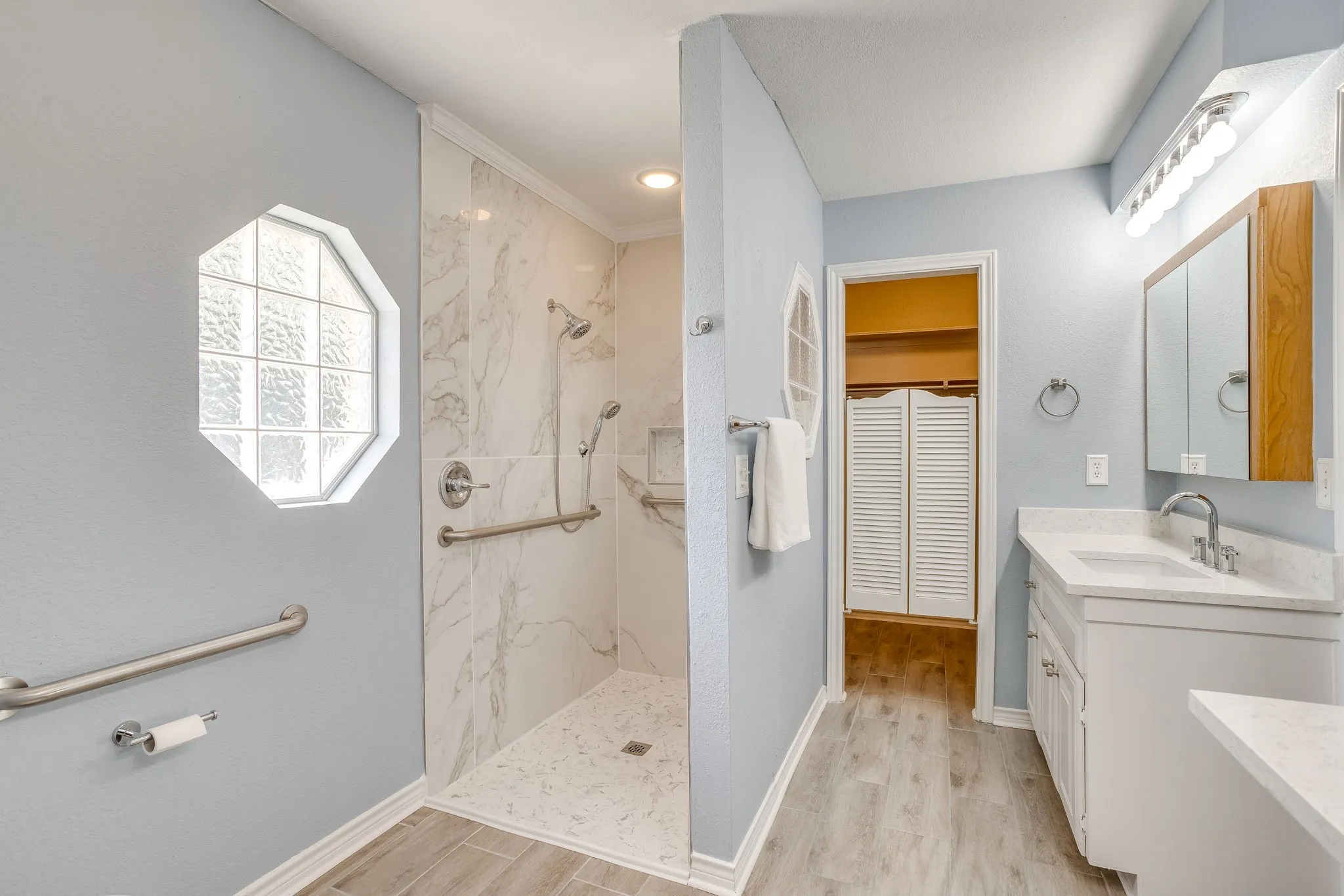 Walk-in shower with grab bars and marble-look tile surround
