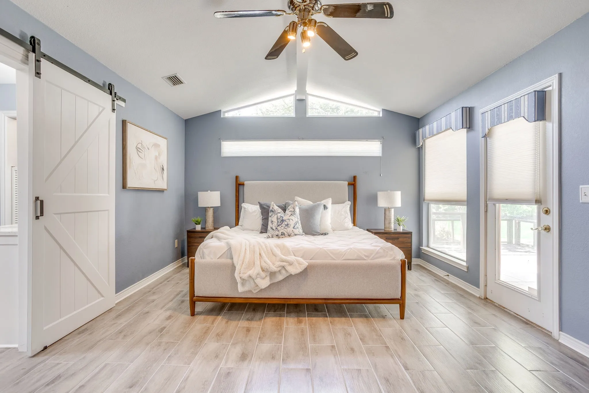 Vaulted ceiling with a ceiling fan, light wood-finish flooring, white barn door, and glass-paneled exterior door