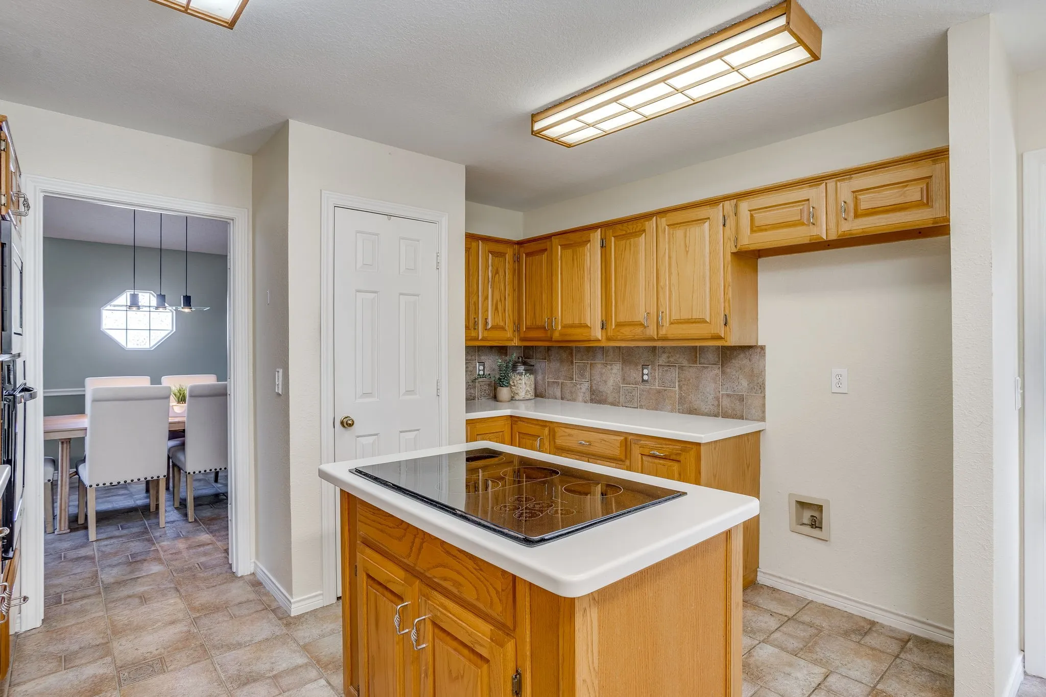 Kitchen featuring wood-finish cabinetry, tile flooring, an island with an integrated cooktop, and a tile backsplash
