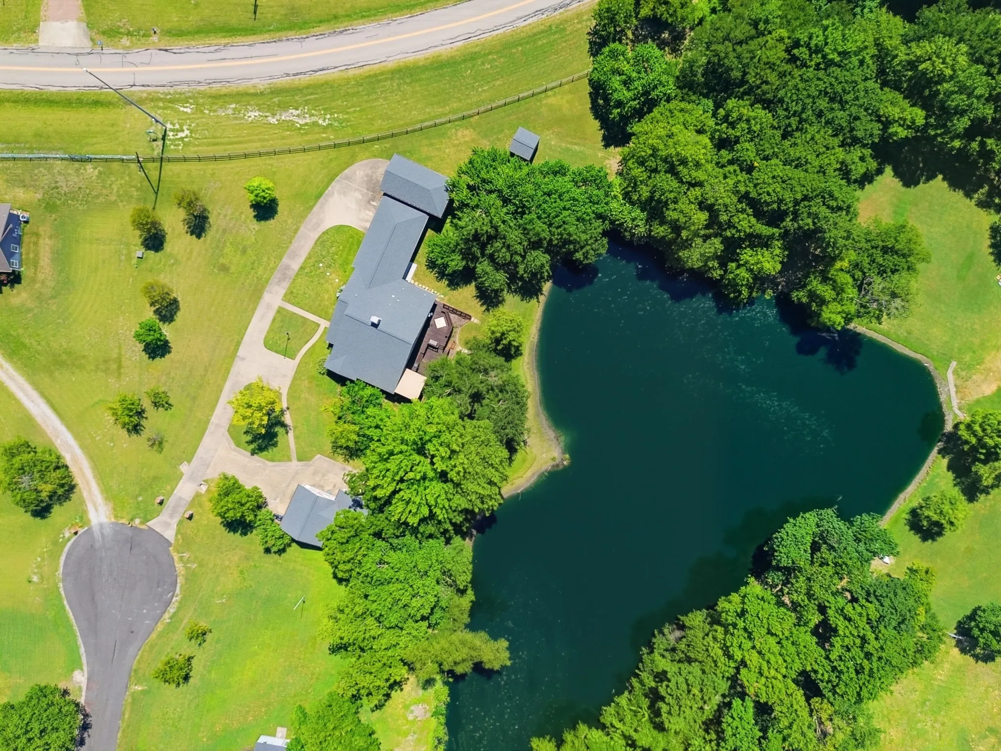 Property featuring a private pond, expansive green space, mature trees, and a paved driveway