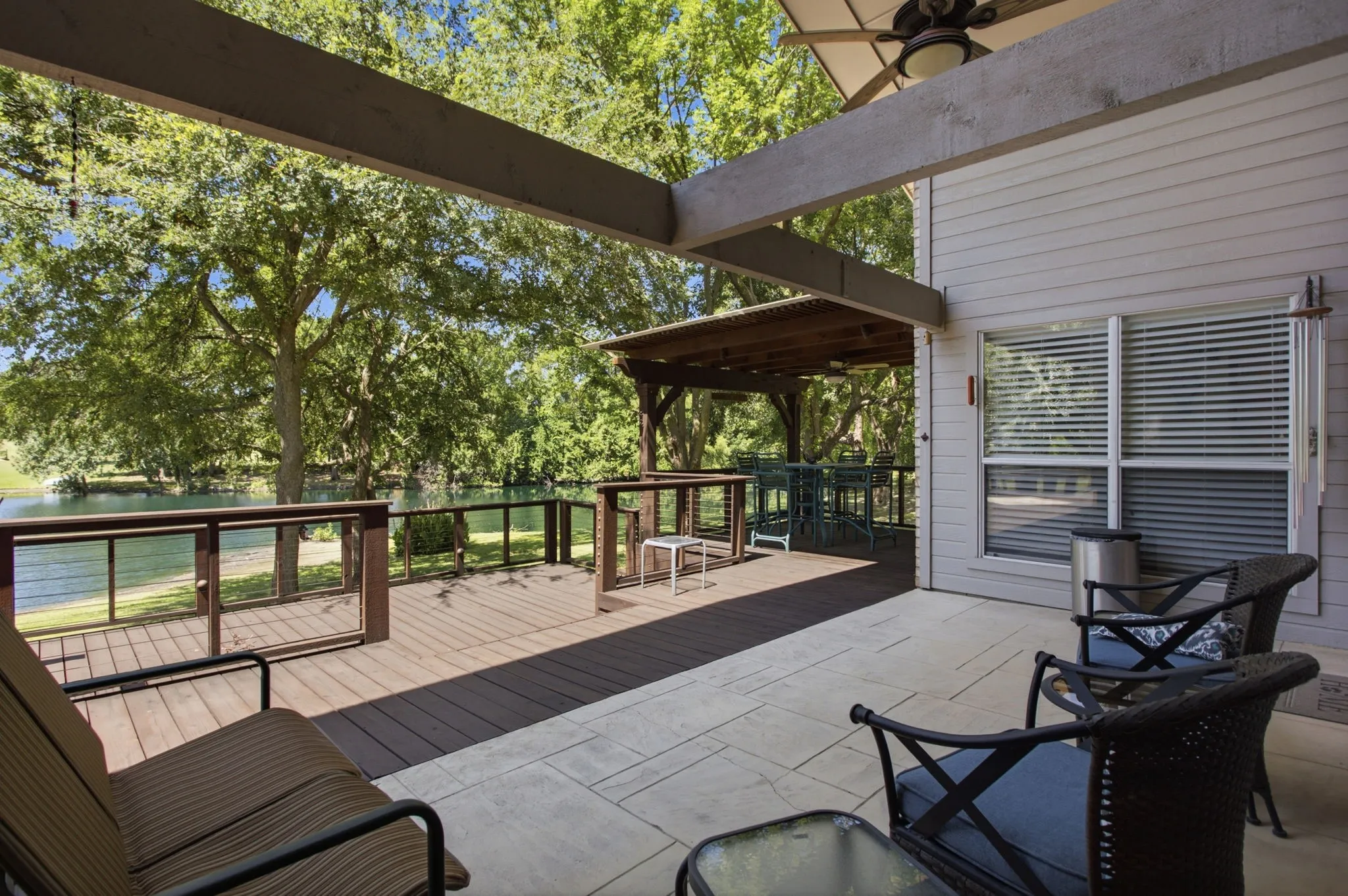 Expansive outdoor living area featuring a covered patio with a ceiling fan, a multi-level wood-finish deck with glass panel railings, and a secondary covered patio with a wood ceiling