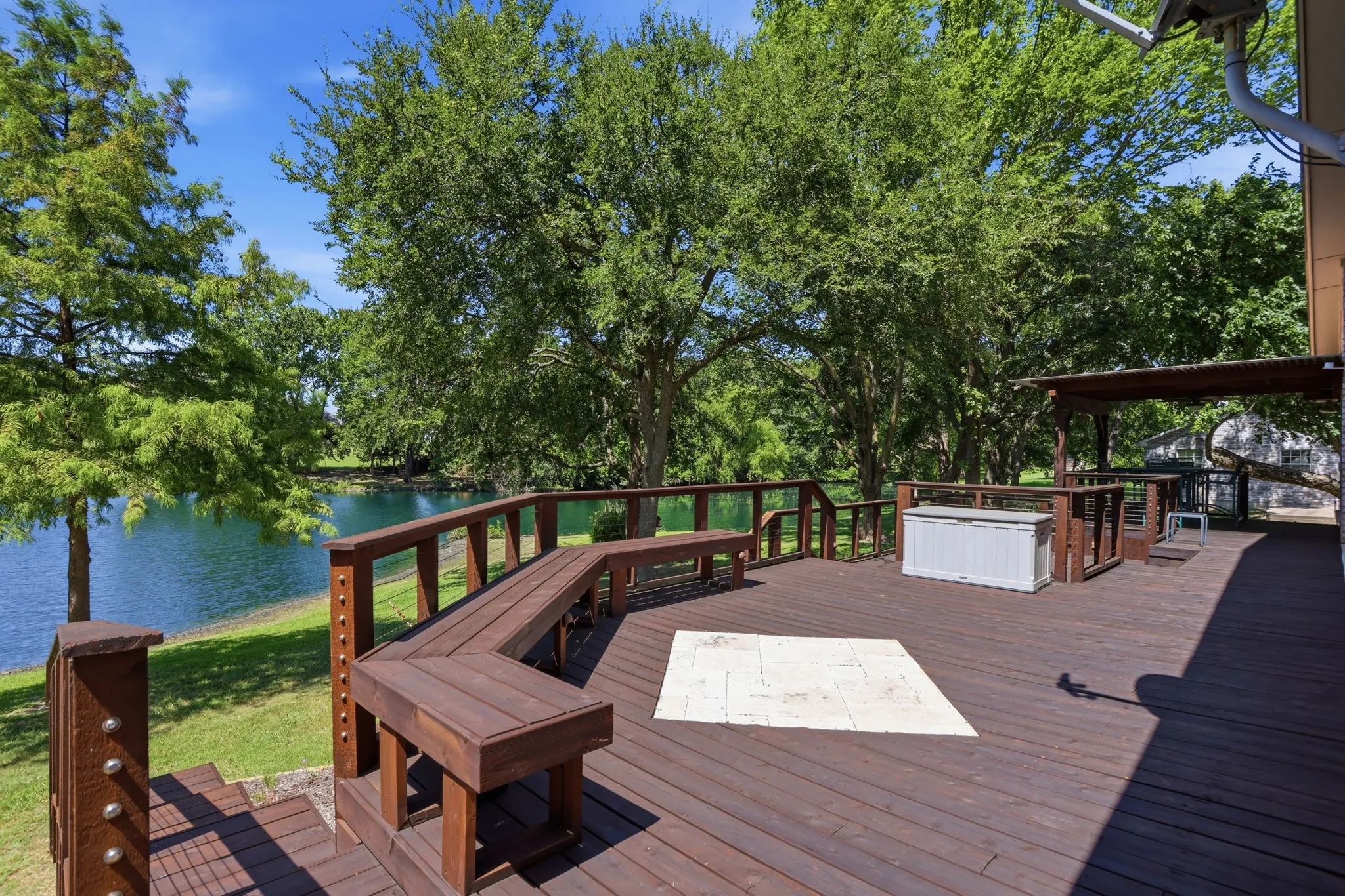 Expansive wood-finish deck with built-in seating, a covered pergola, and direct water frontage