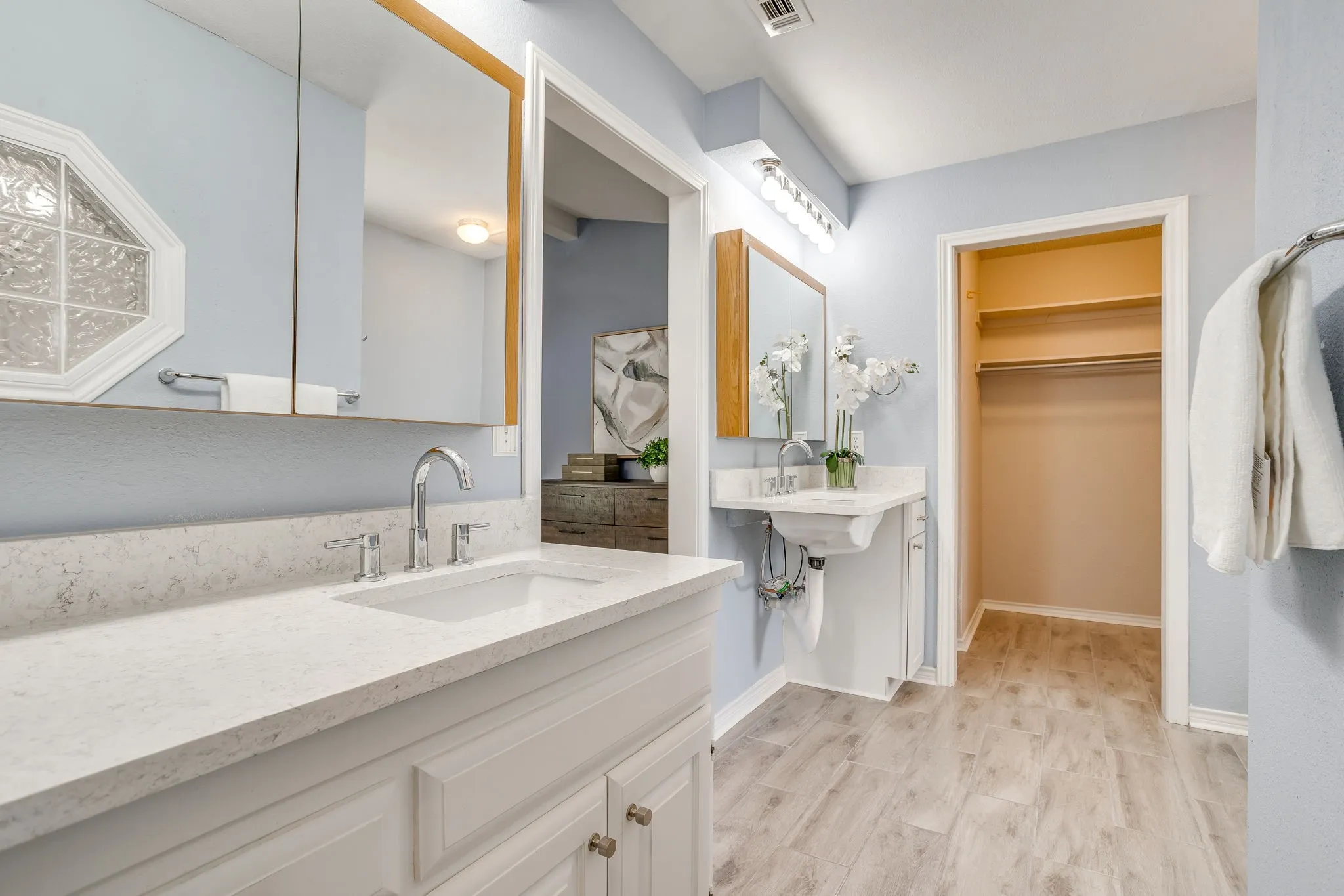 Dual vanity setup with integrated sinks, light-toned wood-finish flooring, and a built-in closet with shelving