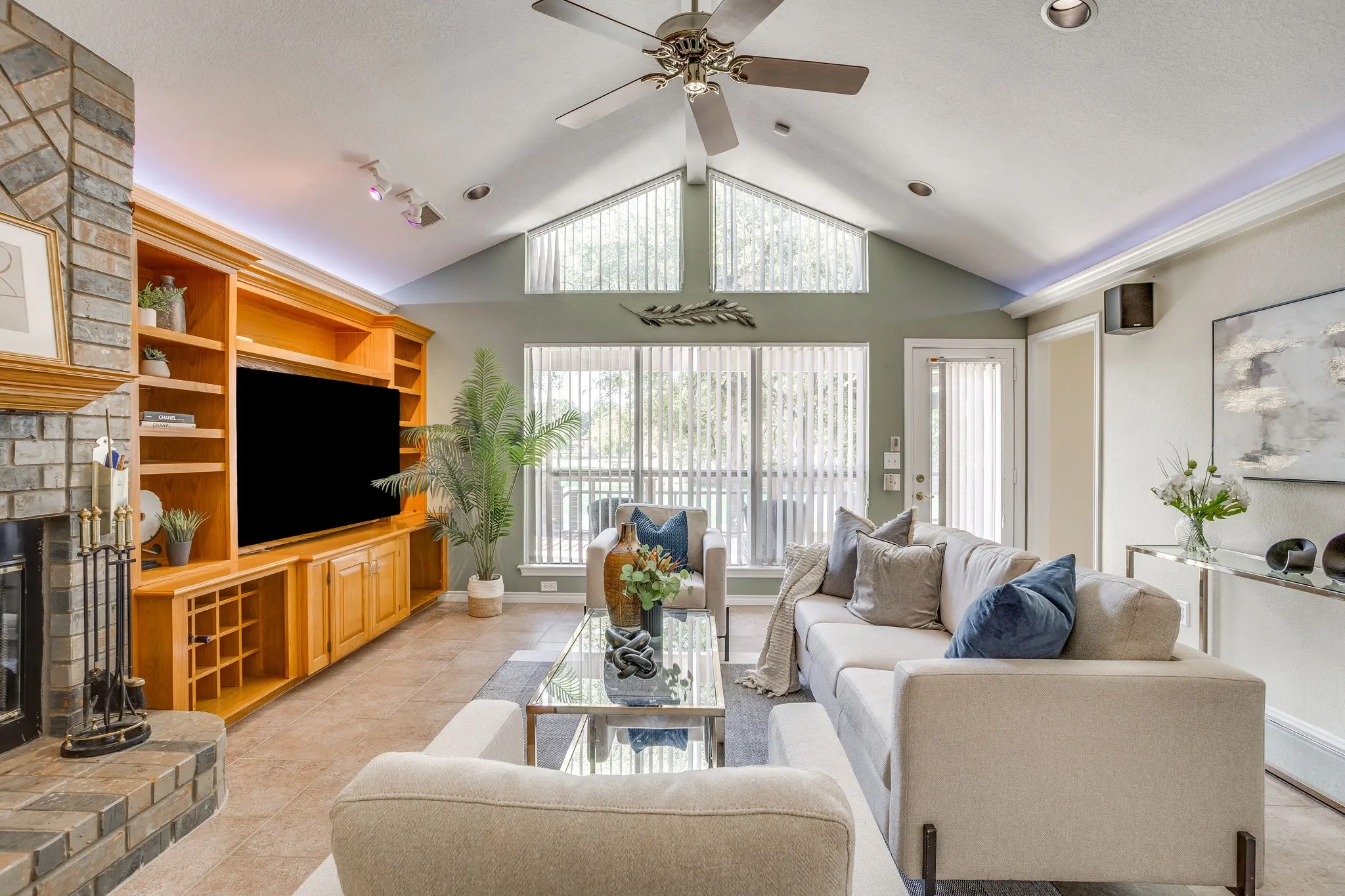 Vaulted ceiling with a ceiling fan, stone-clad fireplace, integrated wood-finish built-in cabinetry, and tile flooring