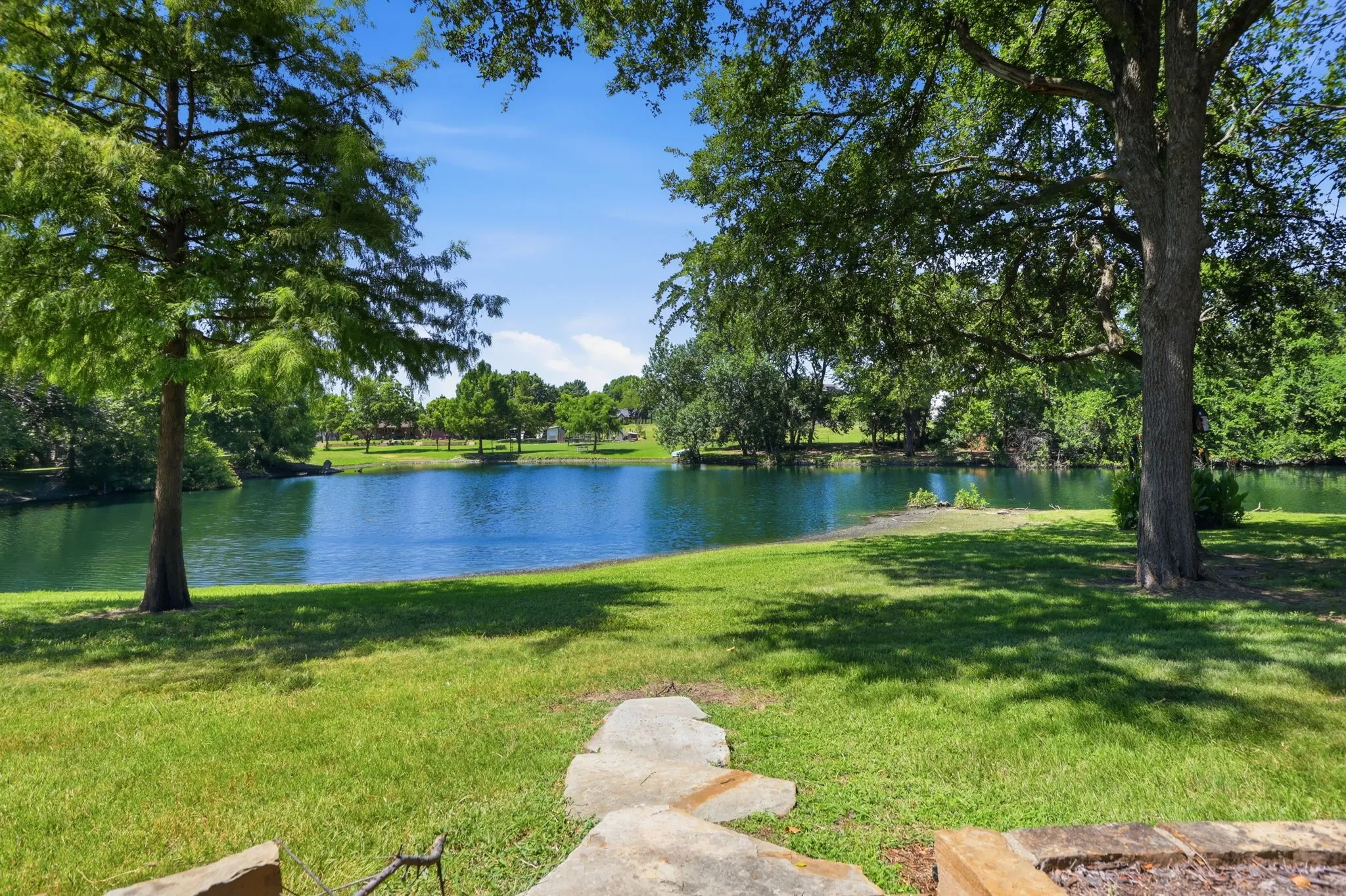 Expansive backyard featuring a manicured lawn, mature trees, and a stone pathway leading to a pond