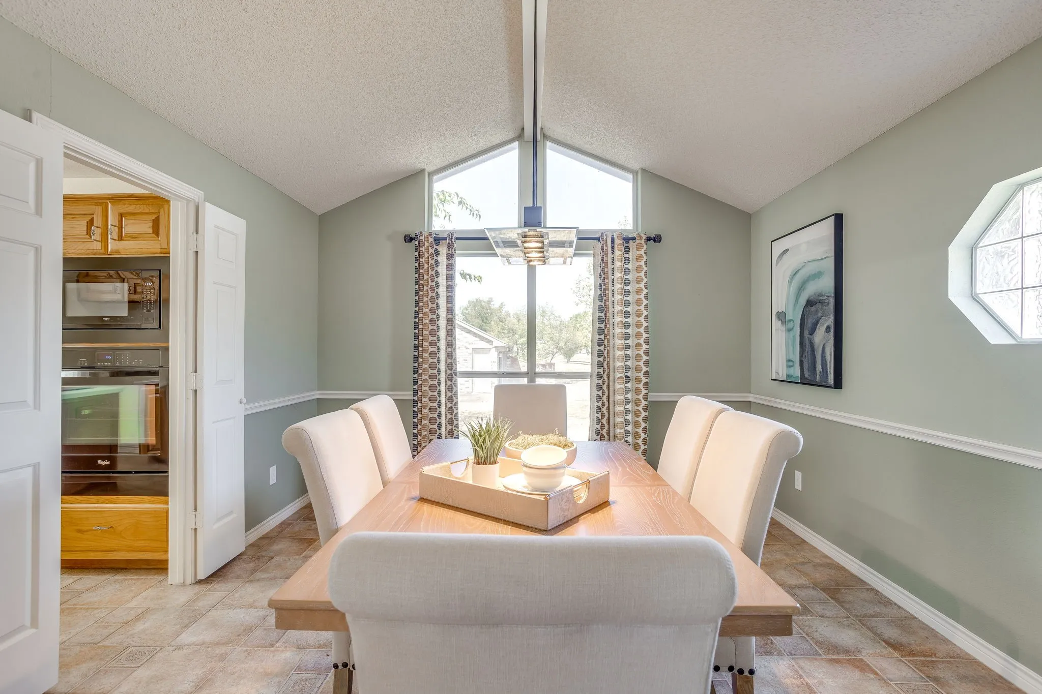 Vaulted ceiling with a linear pendant light fixture, large triangular window, octagon window with textured glass, wood-finish flooring, and a built-in oven and microwave