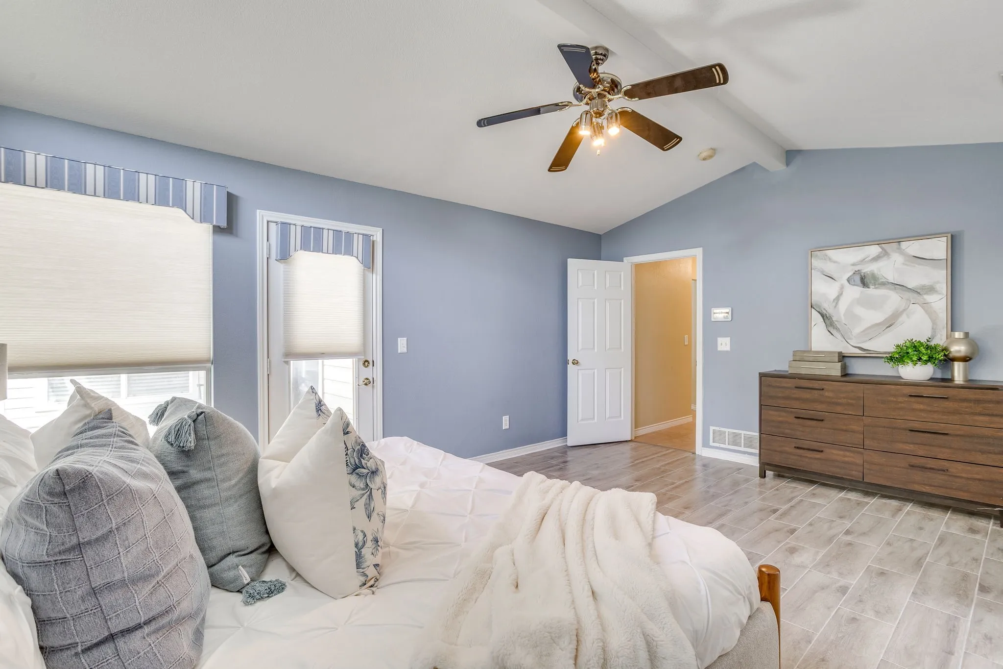 Vaulted ceiling with exposed beam, wood-finish flooring, two windows with valances, and a ceiling fan with light fixture