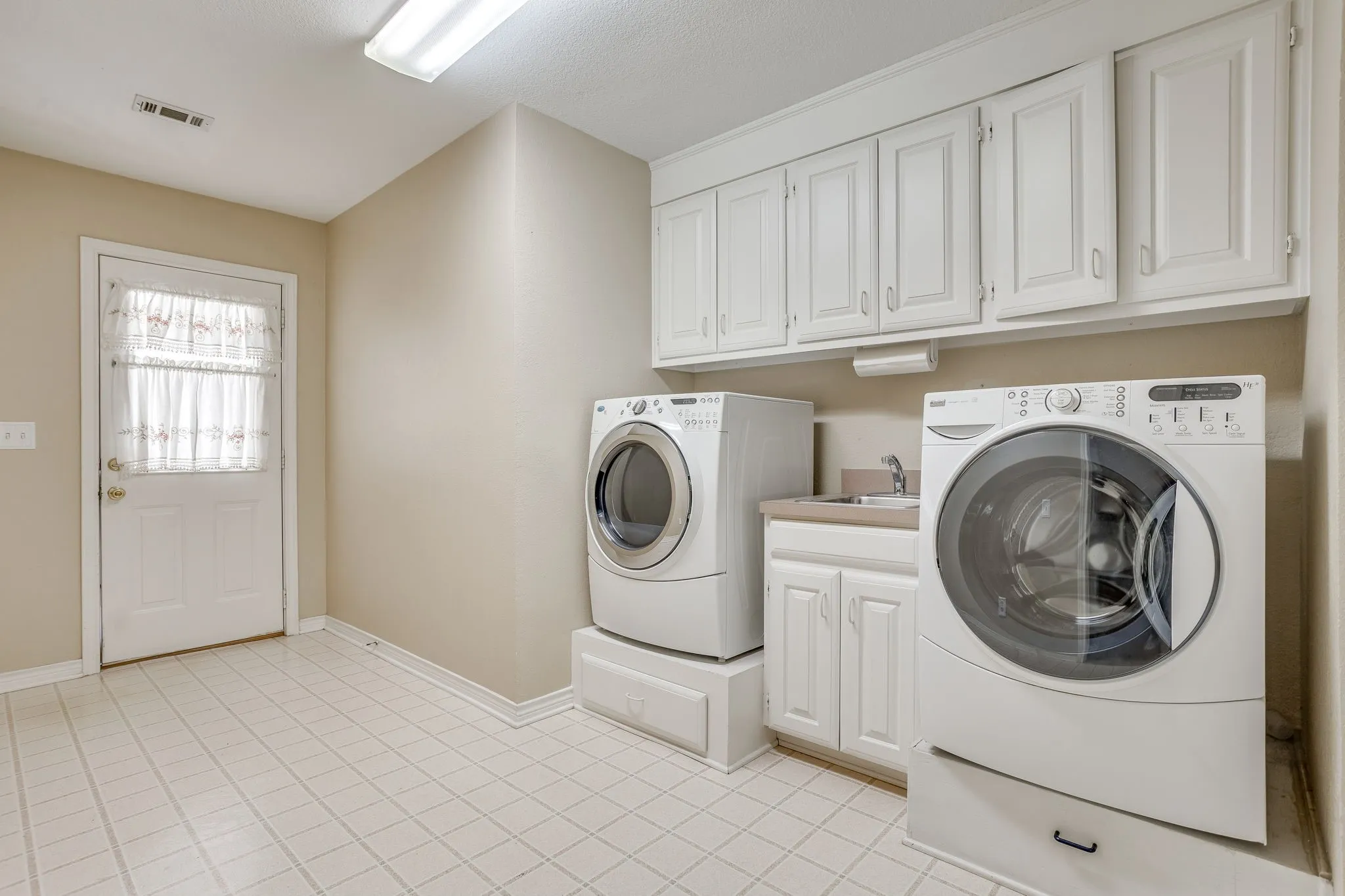 Utility room featuring a built-in sink, white cabinetry, and durable tile flooring