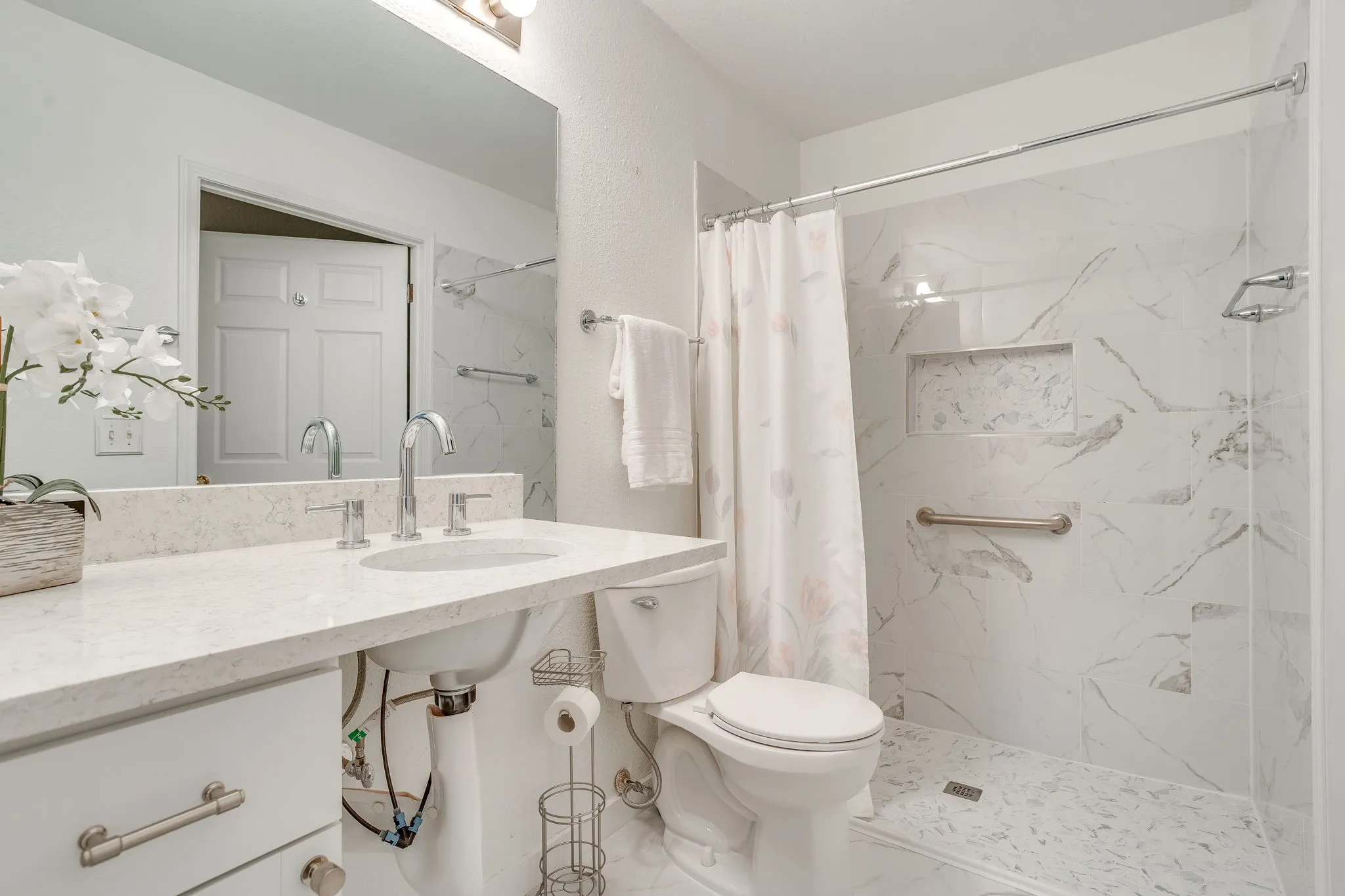 Bathroom featuring a single vanity with a solid surface countertop, chrome fixtures, and a shower with a tiled surround