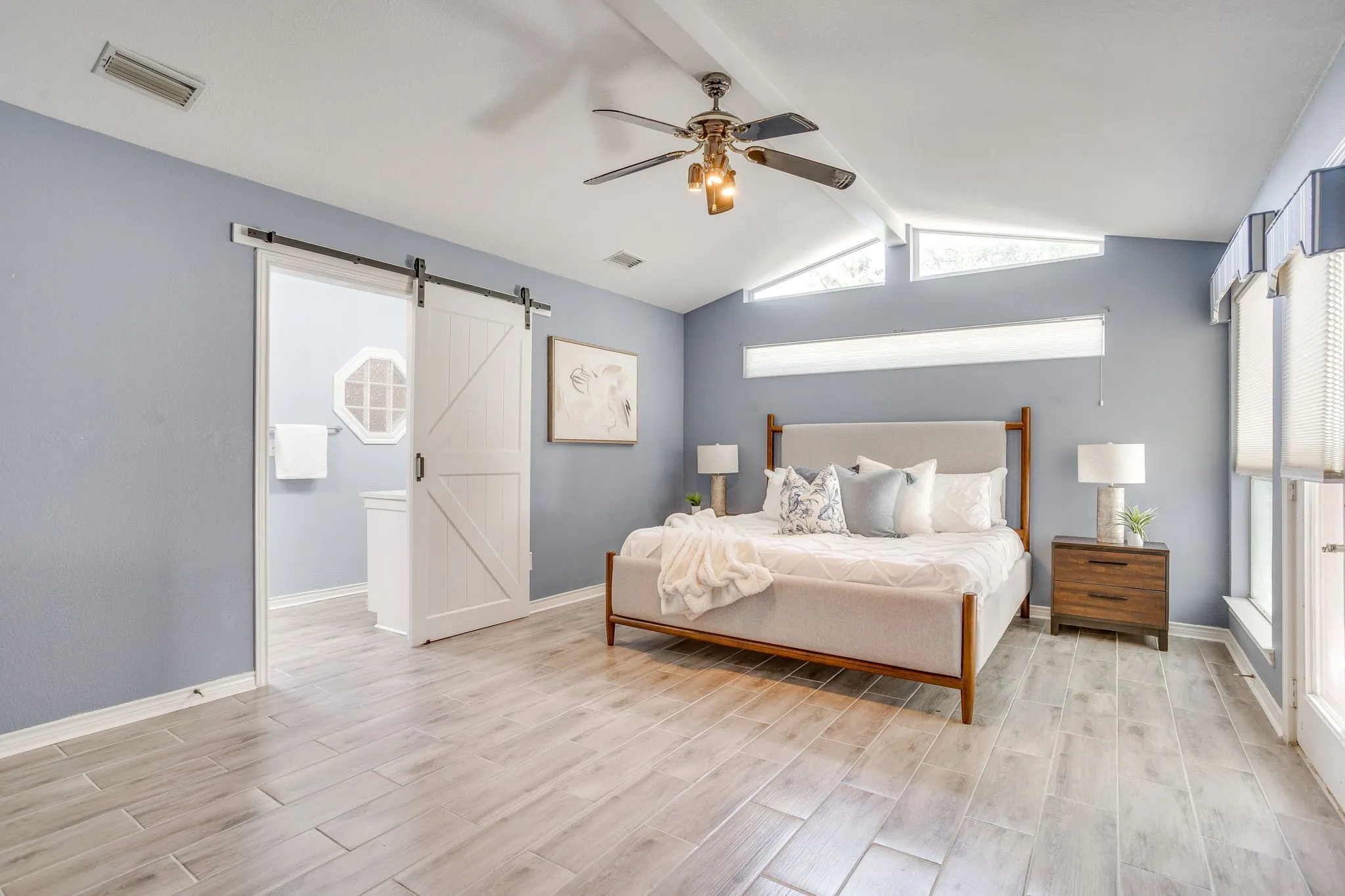 Vaulted ceiling featuring a ceiling fan, wood-finish flooring, white barn door, and a horizontal transom window