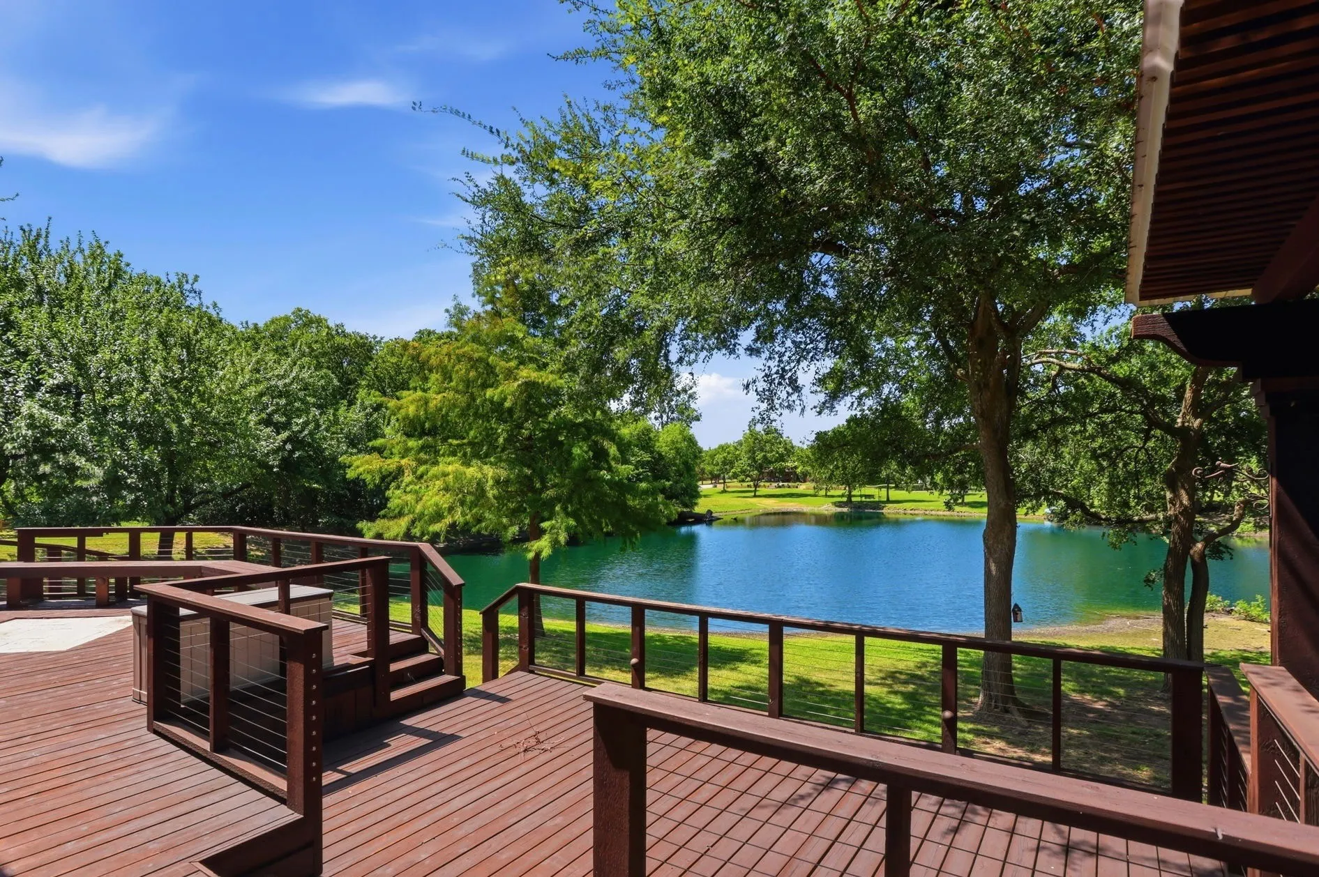 Expansive multi-level wood deck with cable railings and built-in seating overlooking a body of water and mature trees