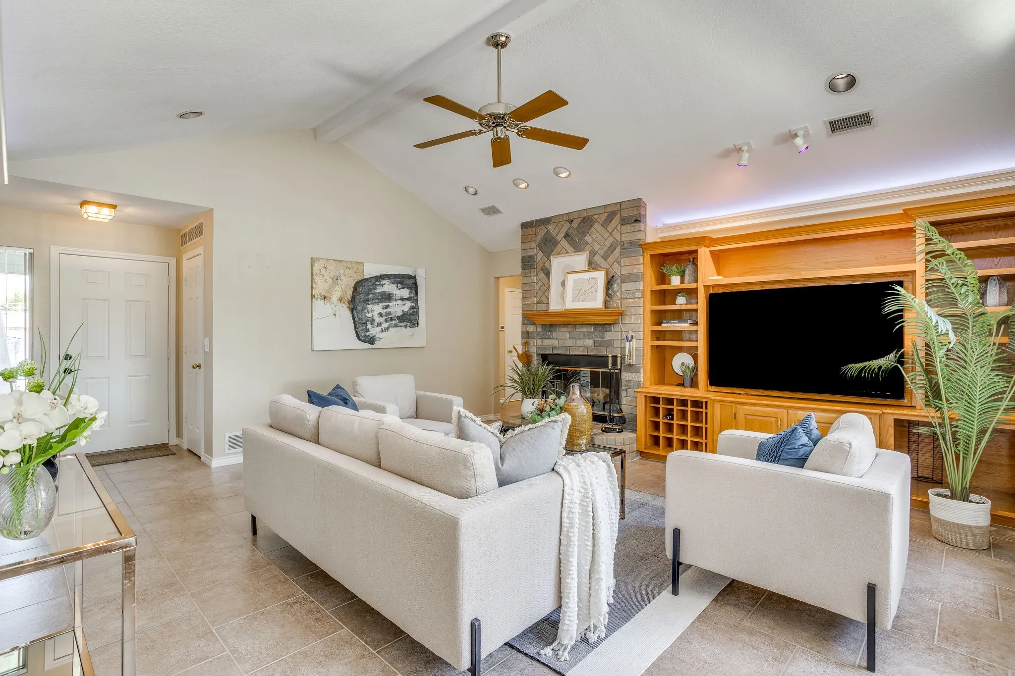 Vaulted ceiling with a ceiling fan, stone-clad fireplace with a wood mantle, custom built-in entertainment center with integrated shelving, tile flooring, and recessed lighting