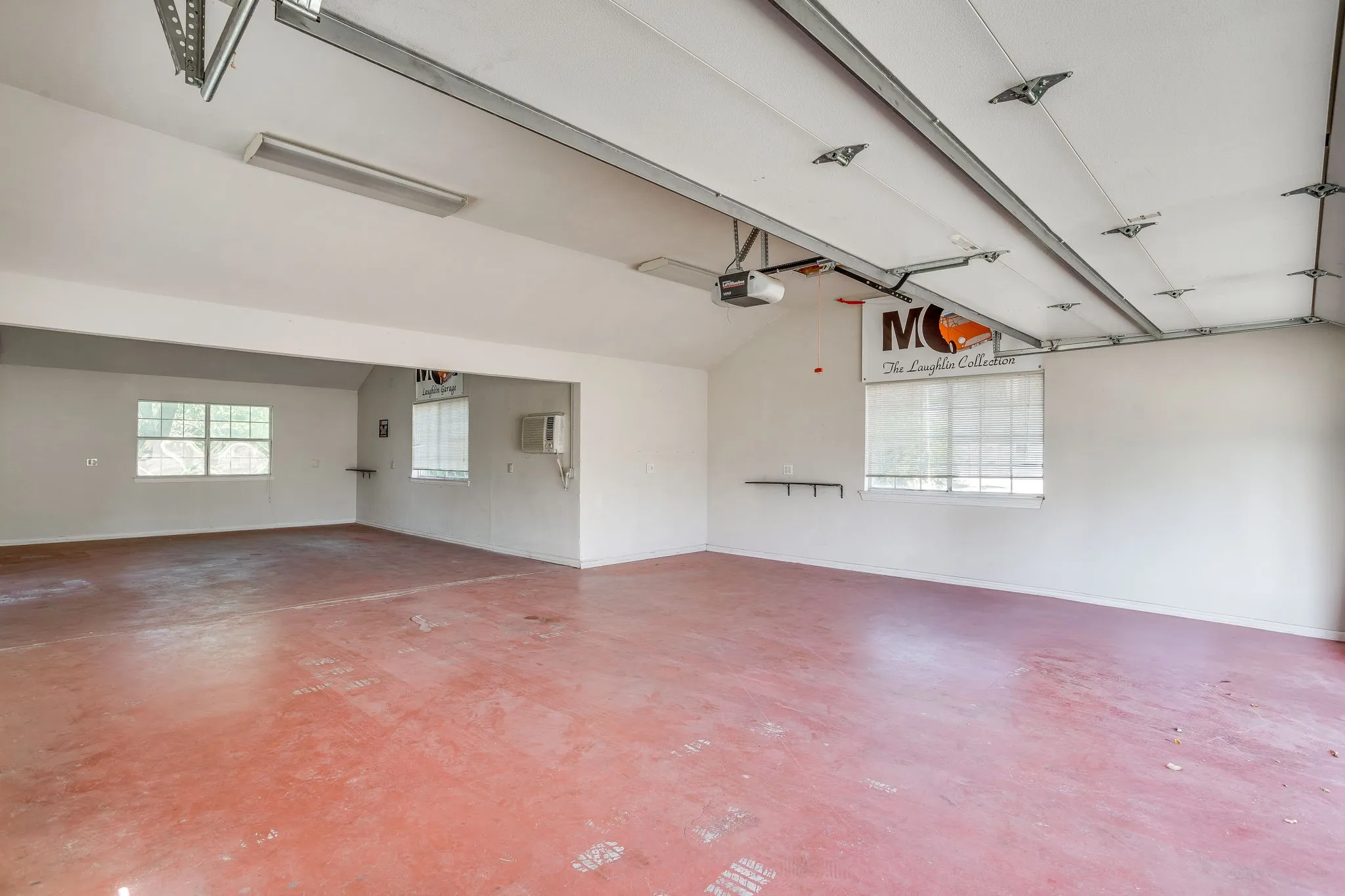 Spacious garage featuring a durable concrete floor, multiple windows for natural light, fluorescent overhead lighting, and an automatic garage door opener