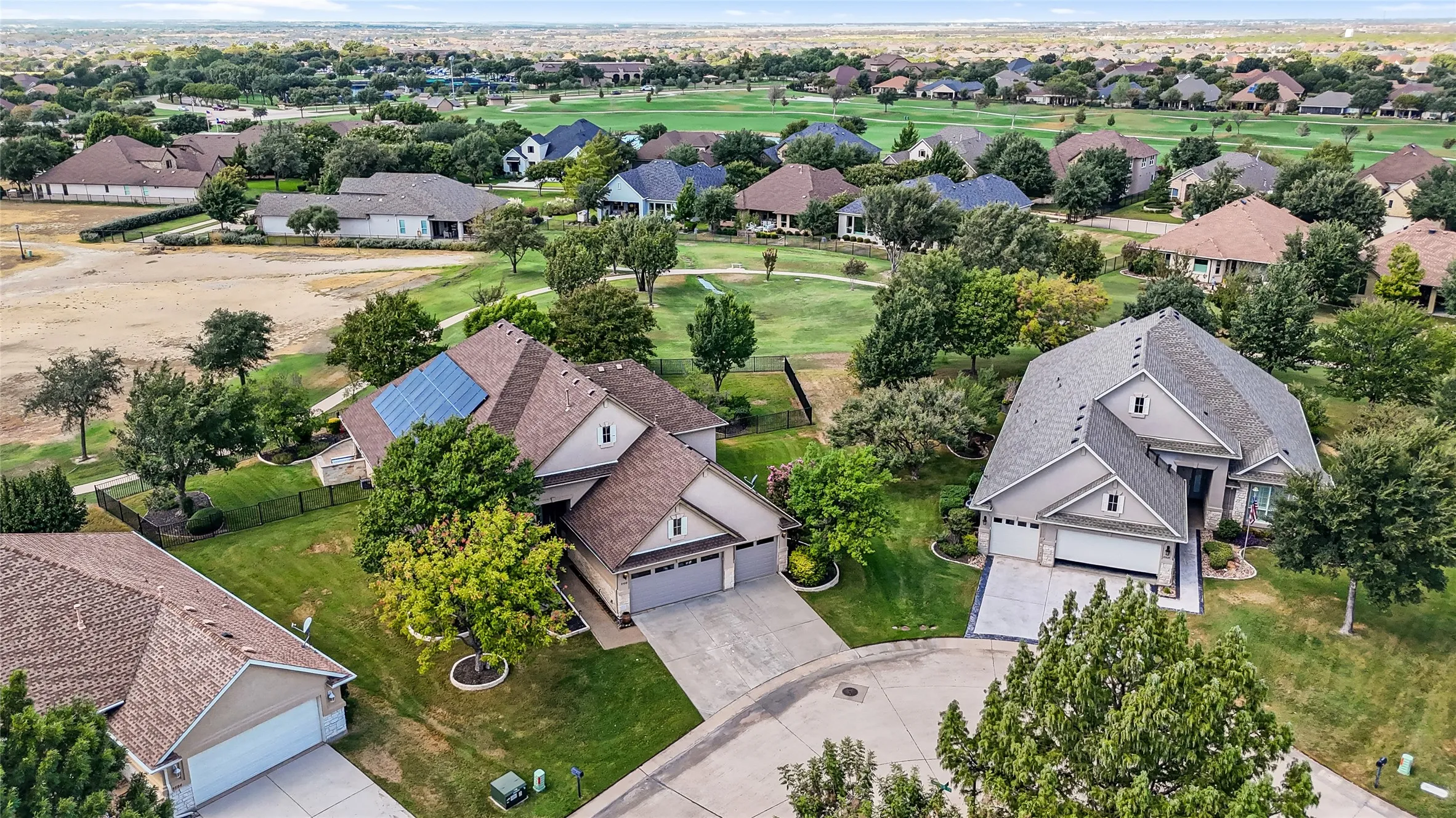 Residential property featuring a shingled roof, solar panel installation, attached two-car garage, and established landscaping