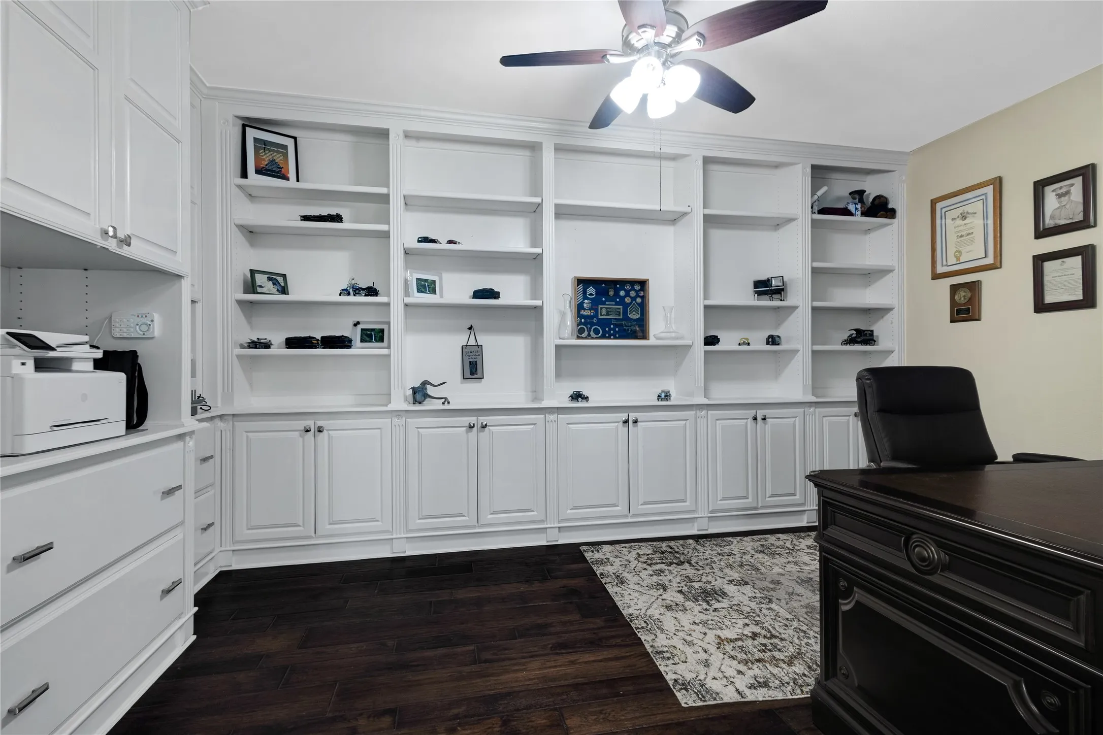 Integrated white cabinetry, extensive built-in shelving, dark wood-finish flooring, and a ceiling fan with integrated lighting